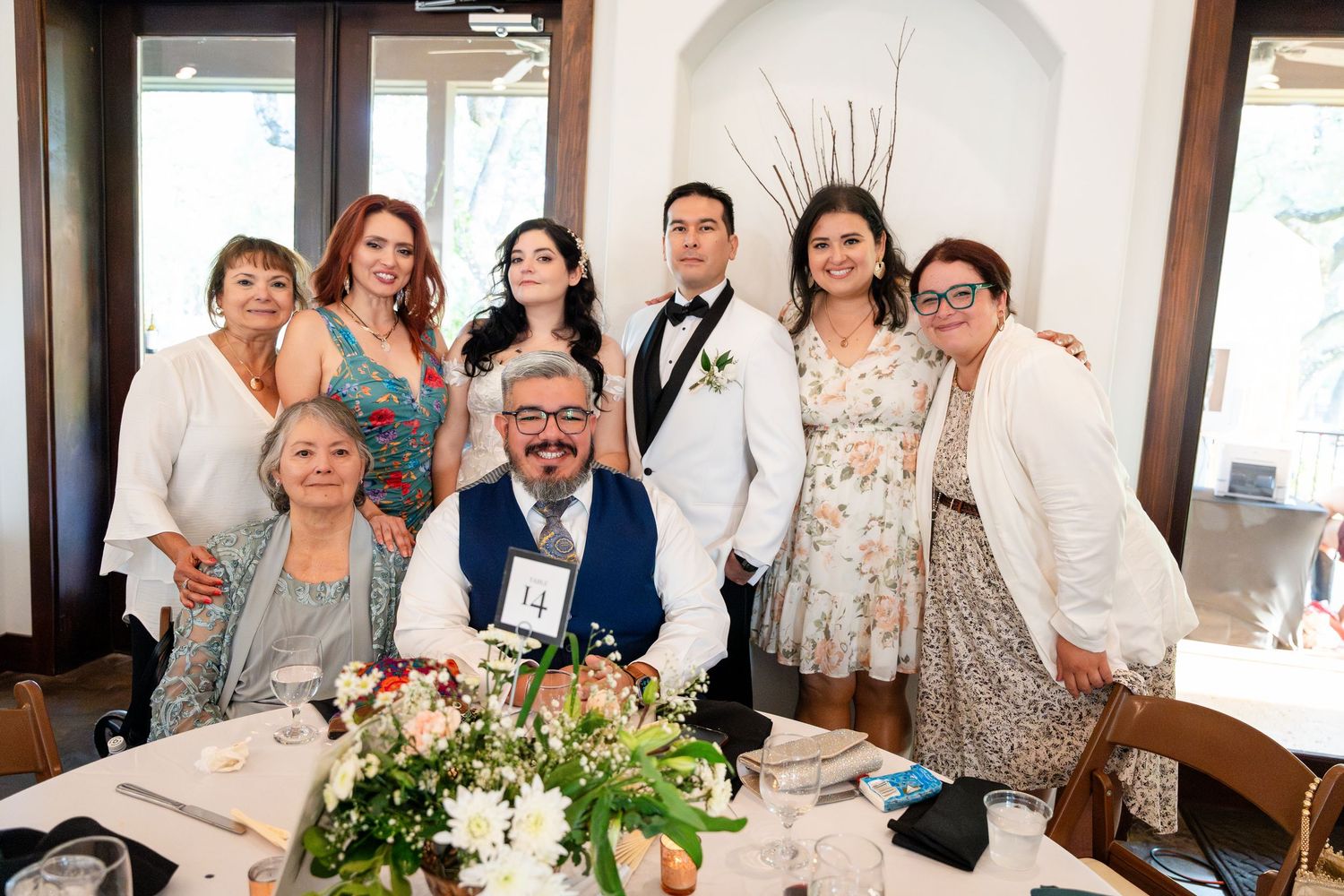 A celebratory gathering of people around a decorated table with floral centerpieces in an elegant indoor setting.