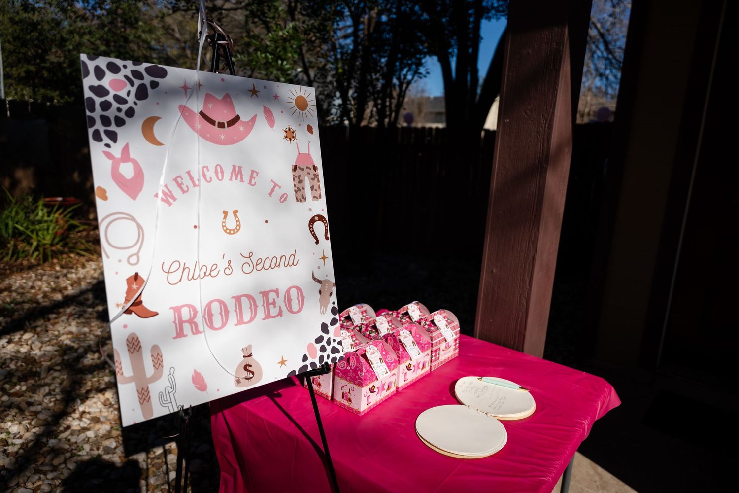 Welcome to Rodeo sign stands near a pink-covered table with white plates at an outdoor western-themed event.
