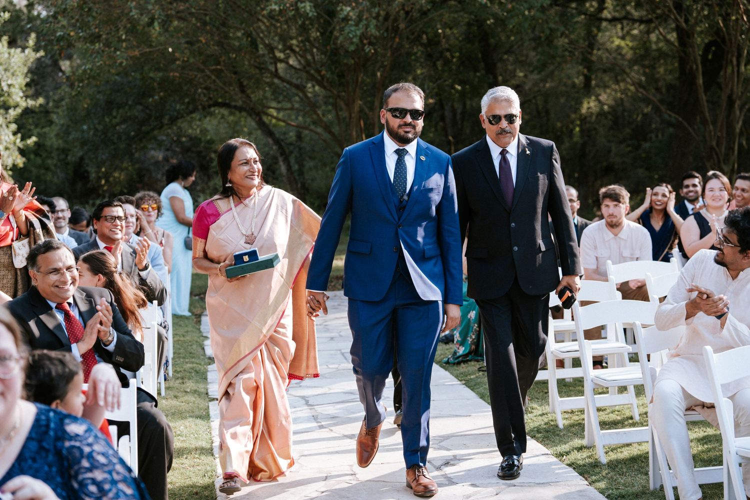 Wedding processional on outdoor white aisle with guests seated on both sides.