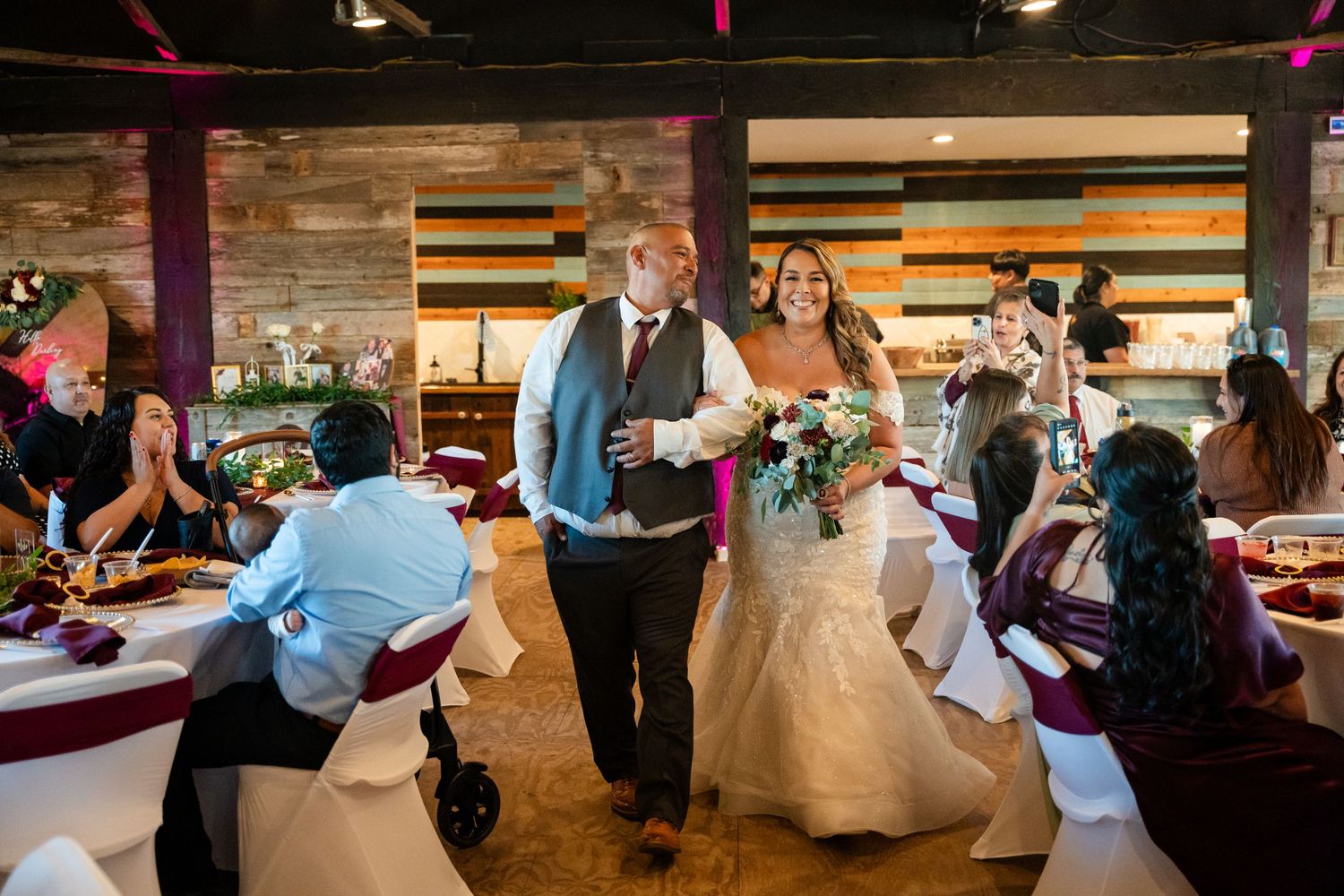 Wedding reception scene with guests celebrating in a rustic venue with wooden walls.