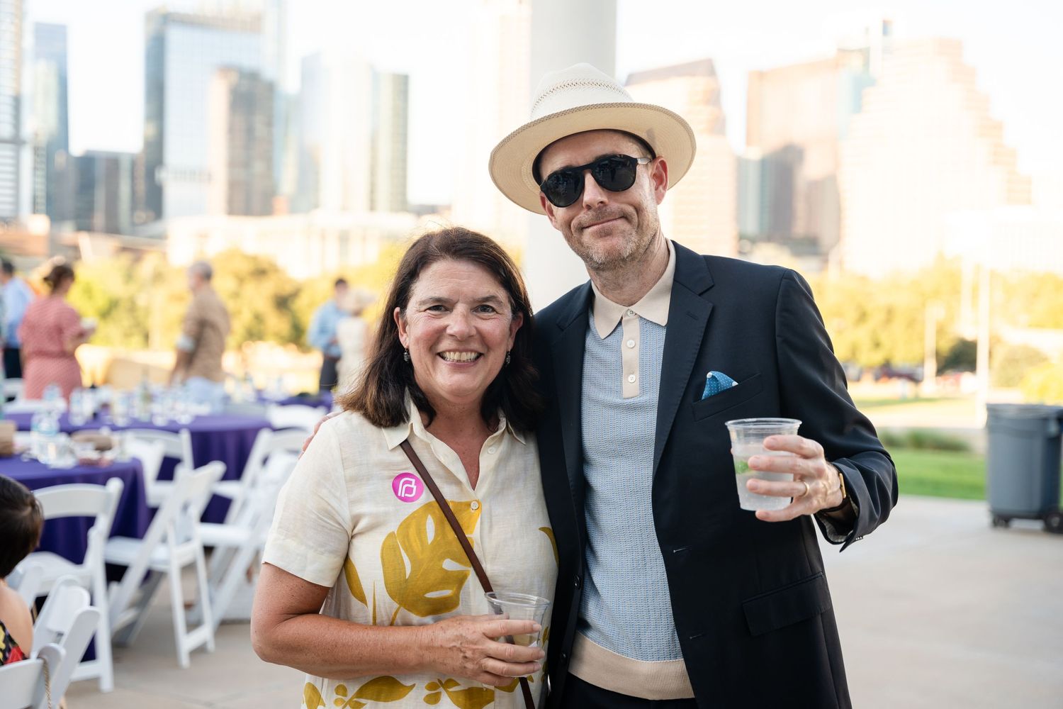Attendees enjoying drinks at outdoor social gathering with urban backdrop.