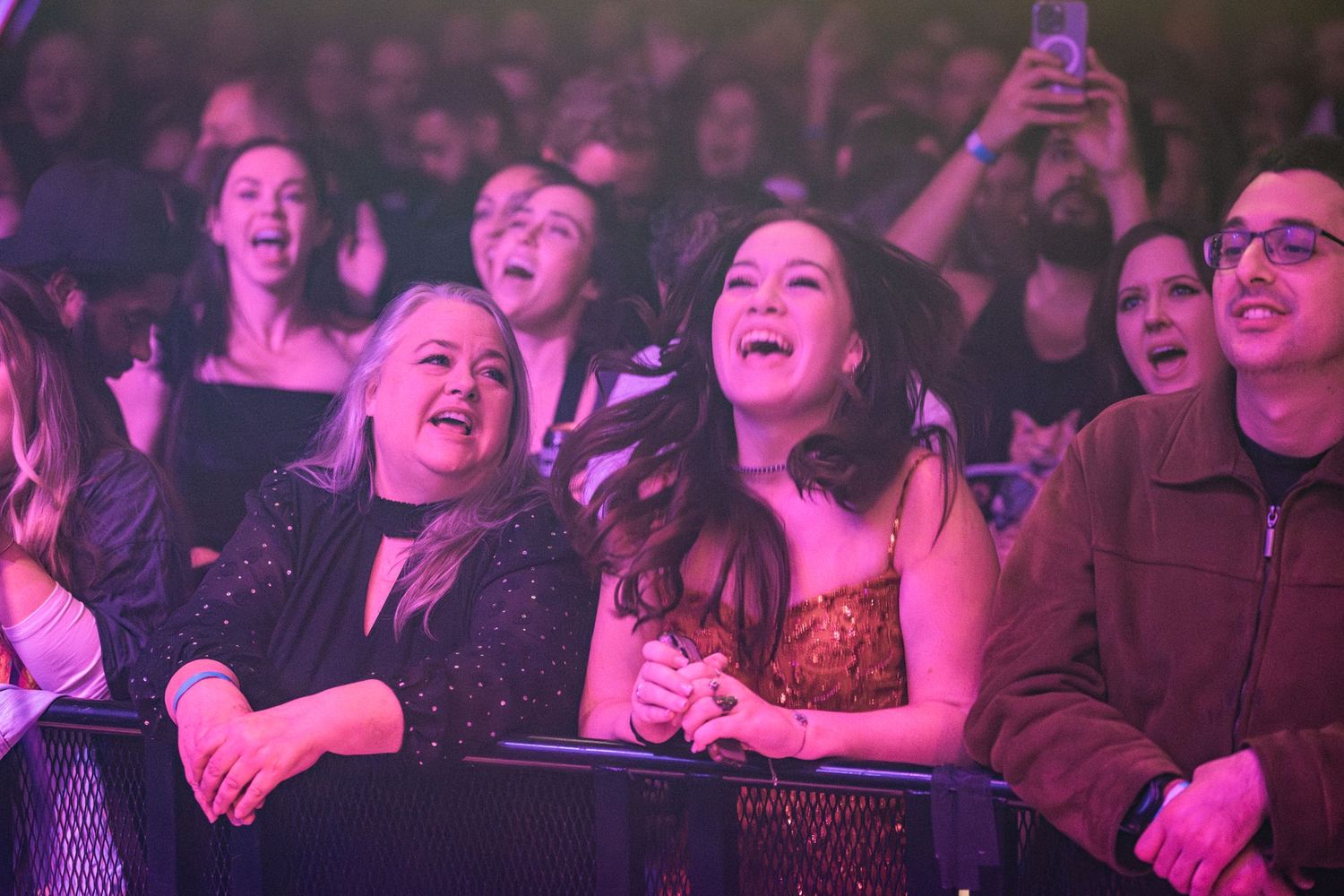Concert attendees singing along and enjoying live music performance with colorful lighting.