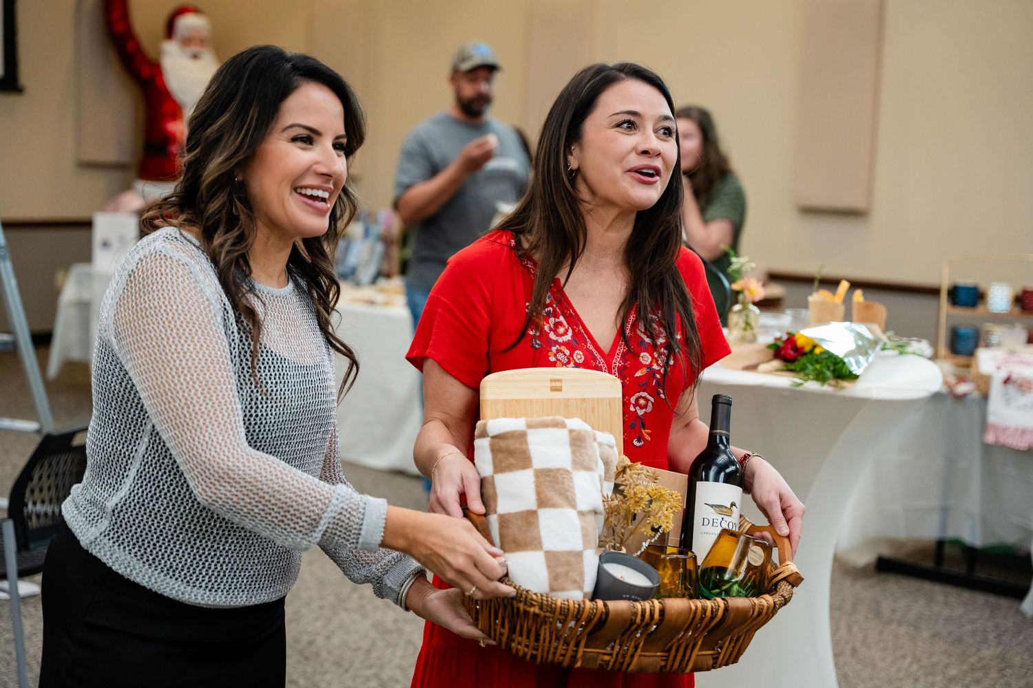 Two people carrying a gift basket at an indoor event.