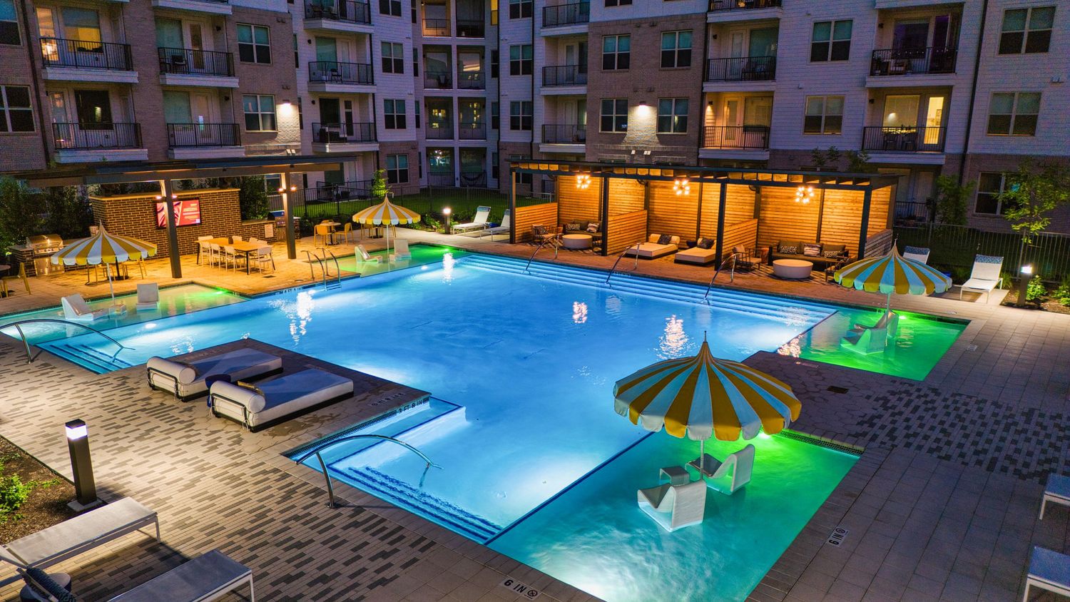 Resort-style pool area featuring curved swimming pools with ambient lighting and covered cabanas at twilight.