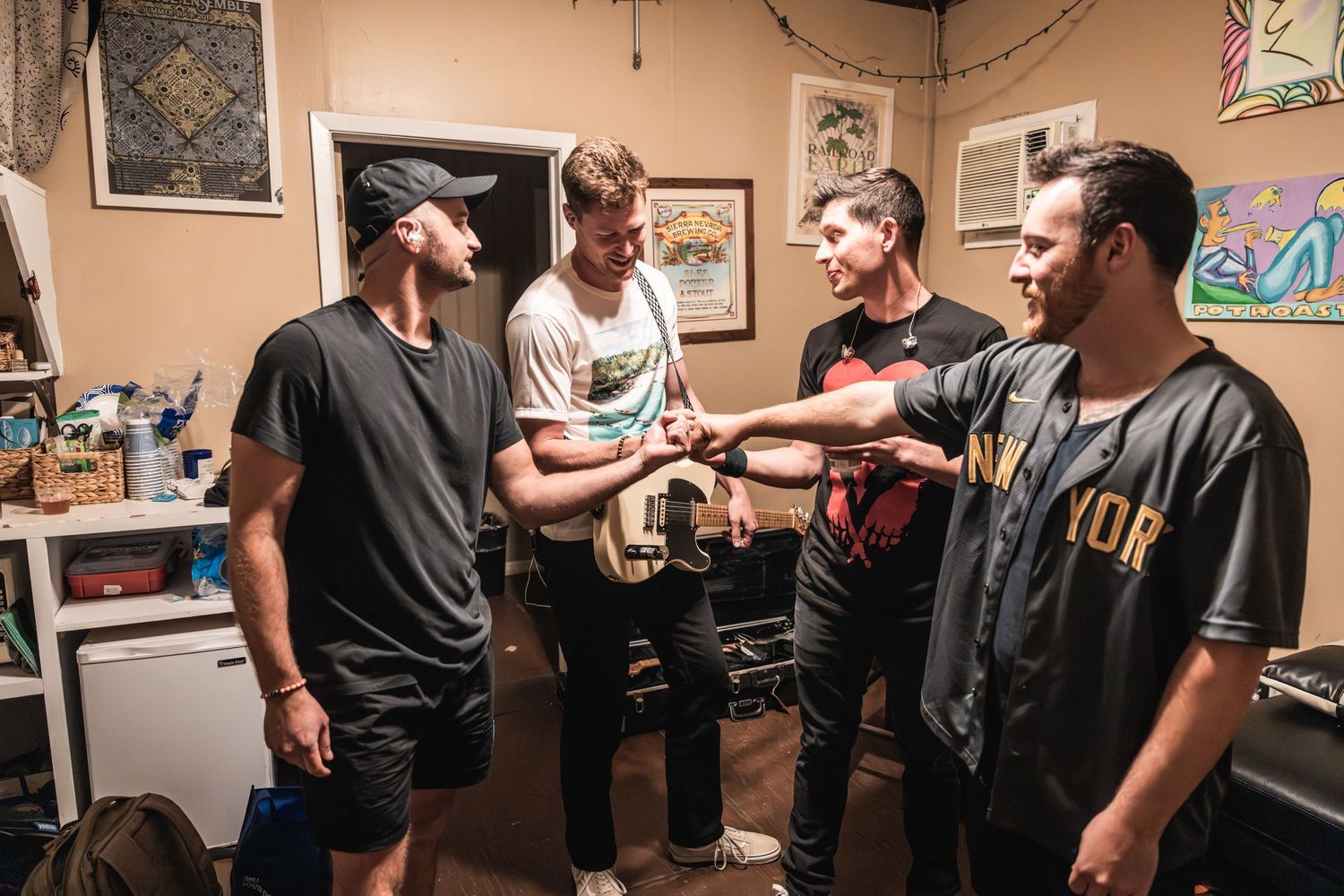 Four band members gather backstage in a small room discussing music and the upcoming show.