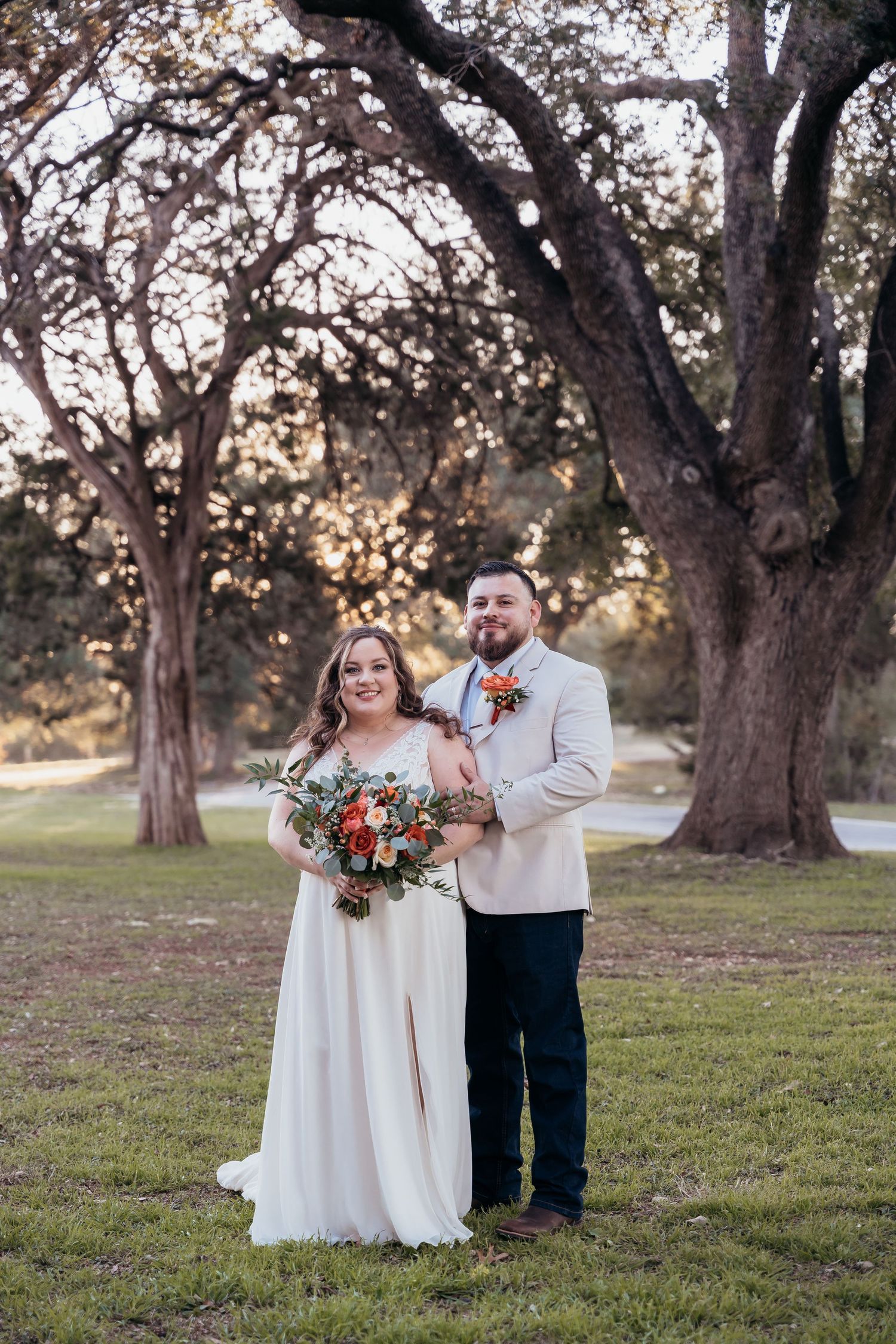 A couple stands among large oak trees during sunset for their wedding photos.
