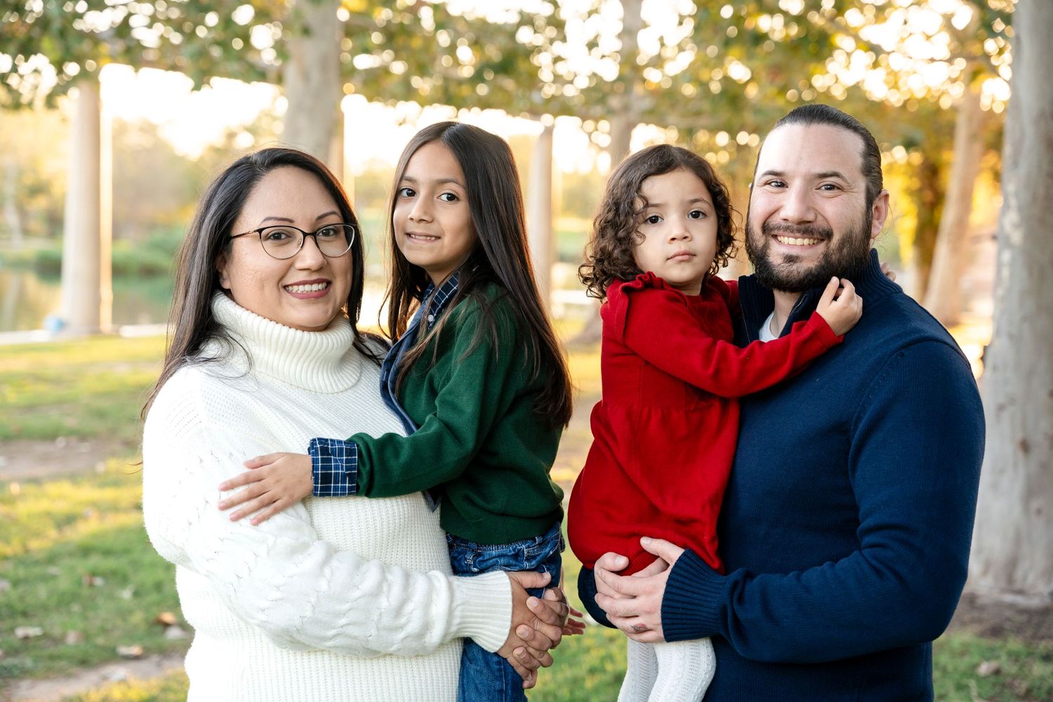 Happy family of four posing together outdoors during sunset with bokeh background.