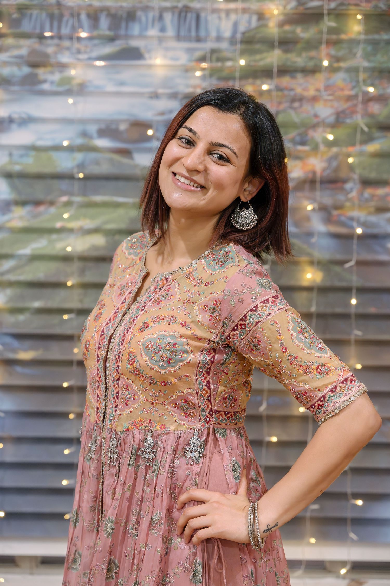A person in a pink embroidered dress poses against a backdrop with twinkling lights.