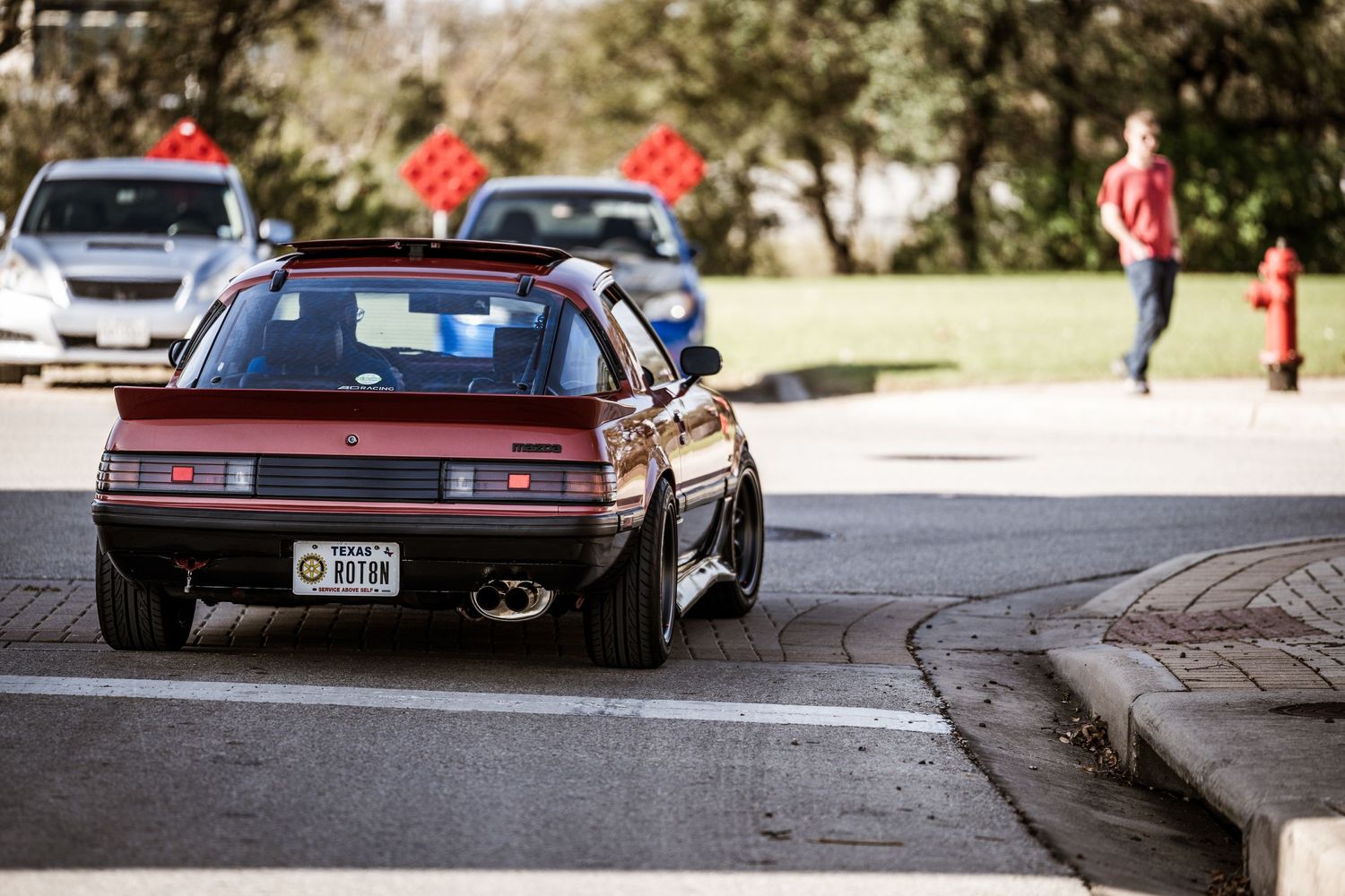 Maroon sports car driving past on a street with red traffic signs visible.