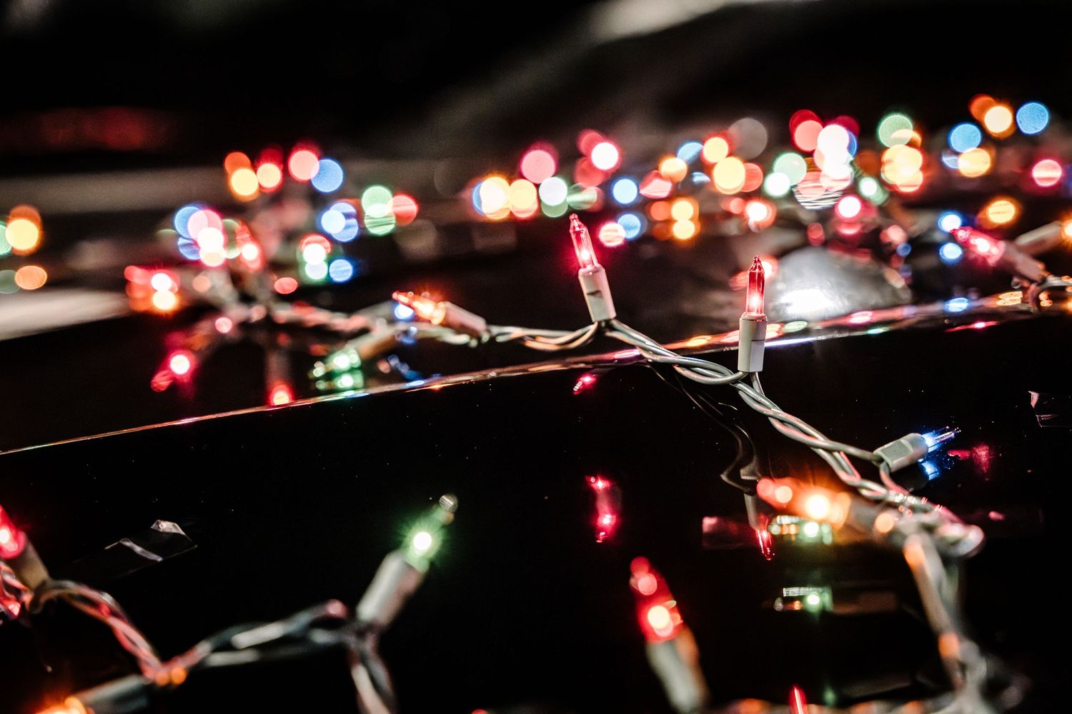 Colorful string lights creating bokeh effect at nighttime car event.