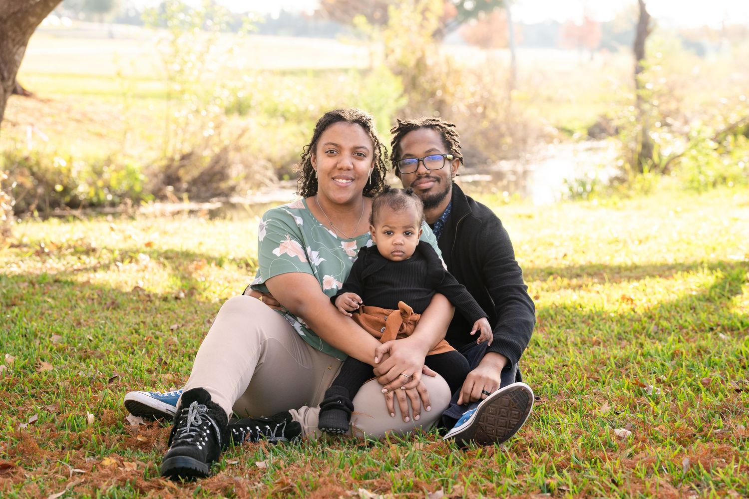 A family seated together on grass during an autumn outdoor photo session.