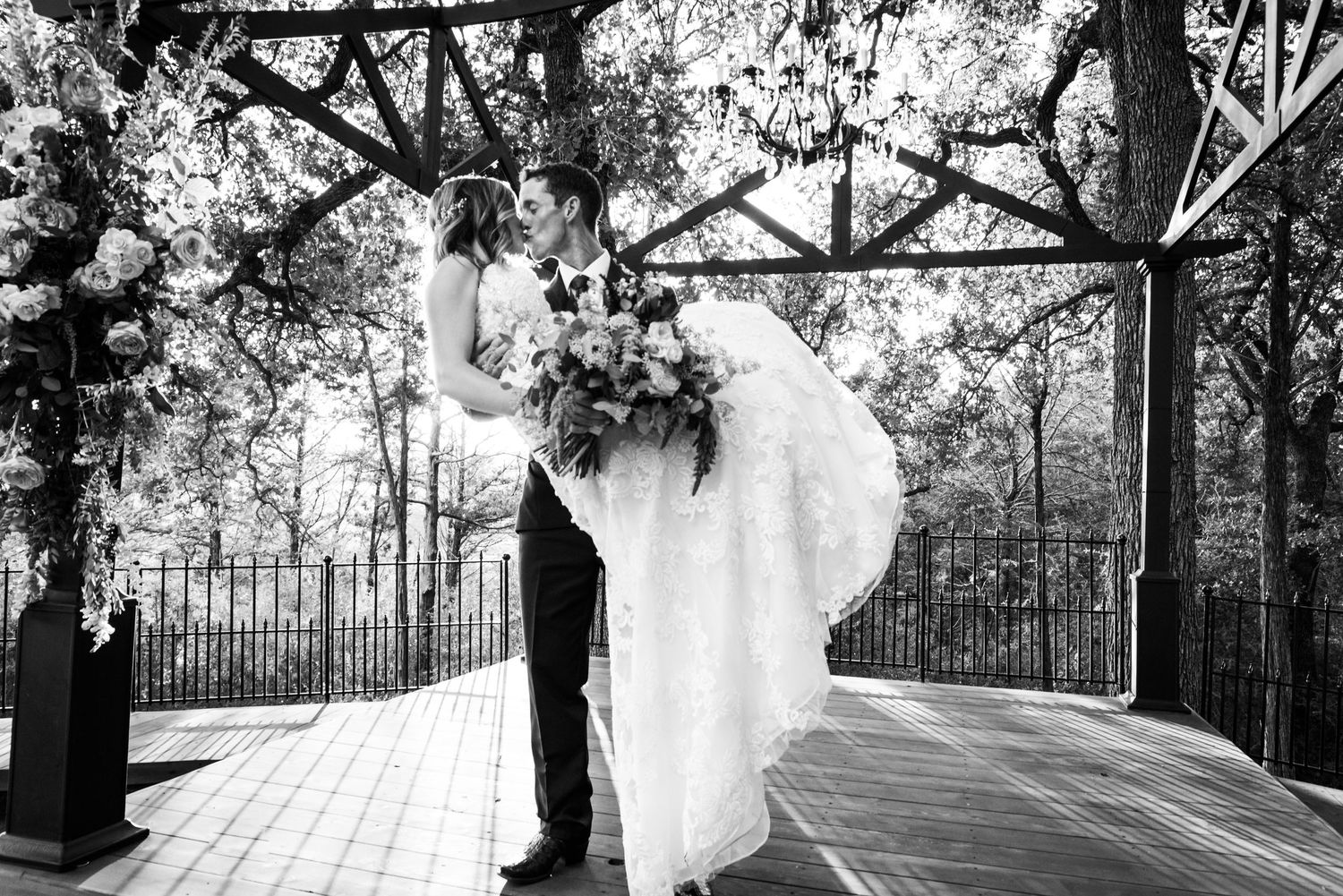 A dramatic black and white wedding portrait showing a romantic dip kiss on an outdoor deck.