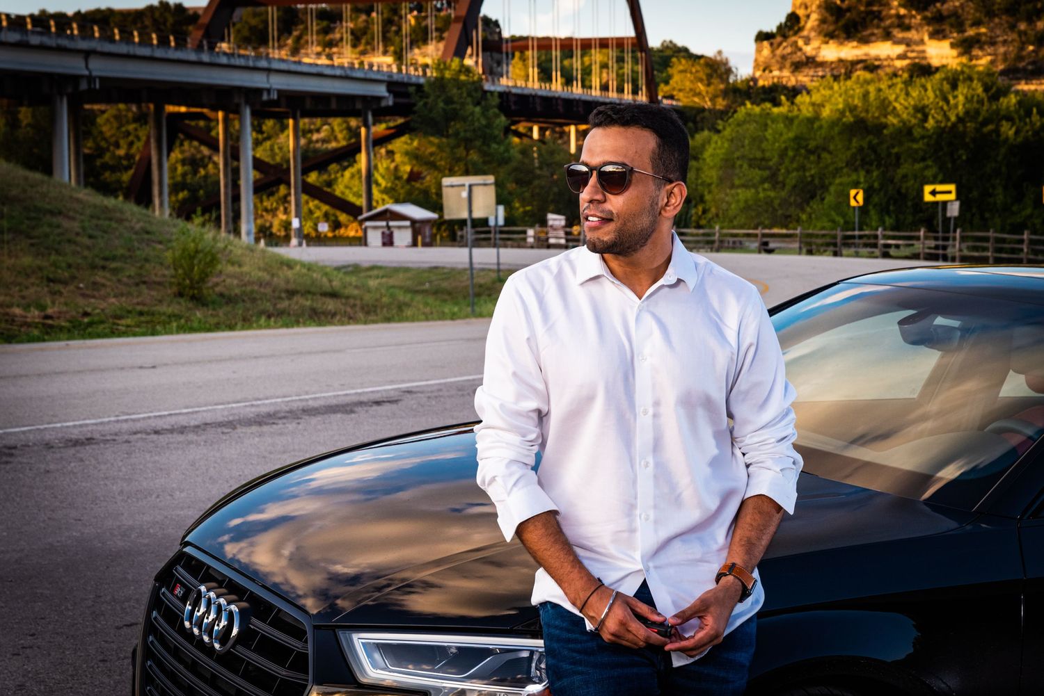 Stylish black Audi parked near bridge during sunset with dramatic lighting.