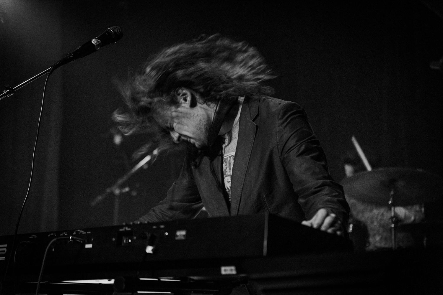 A musician plays keyboard on stage in dramatic dark lighting during a performance.