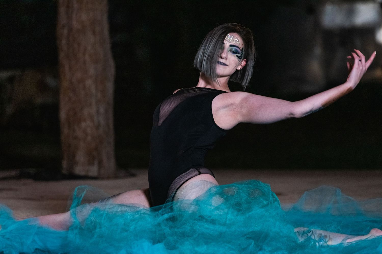Performer in black outfit poses dramatically on blue fabric during artistic performance.