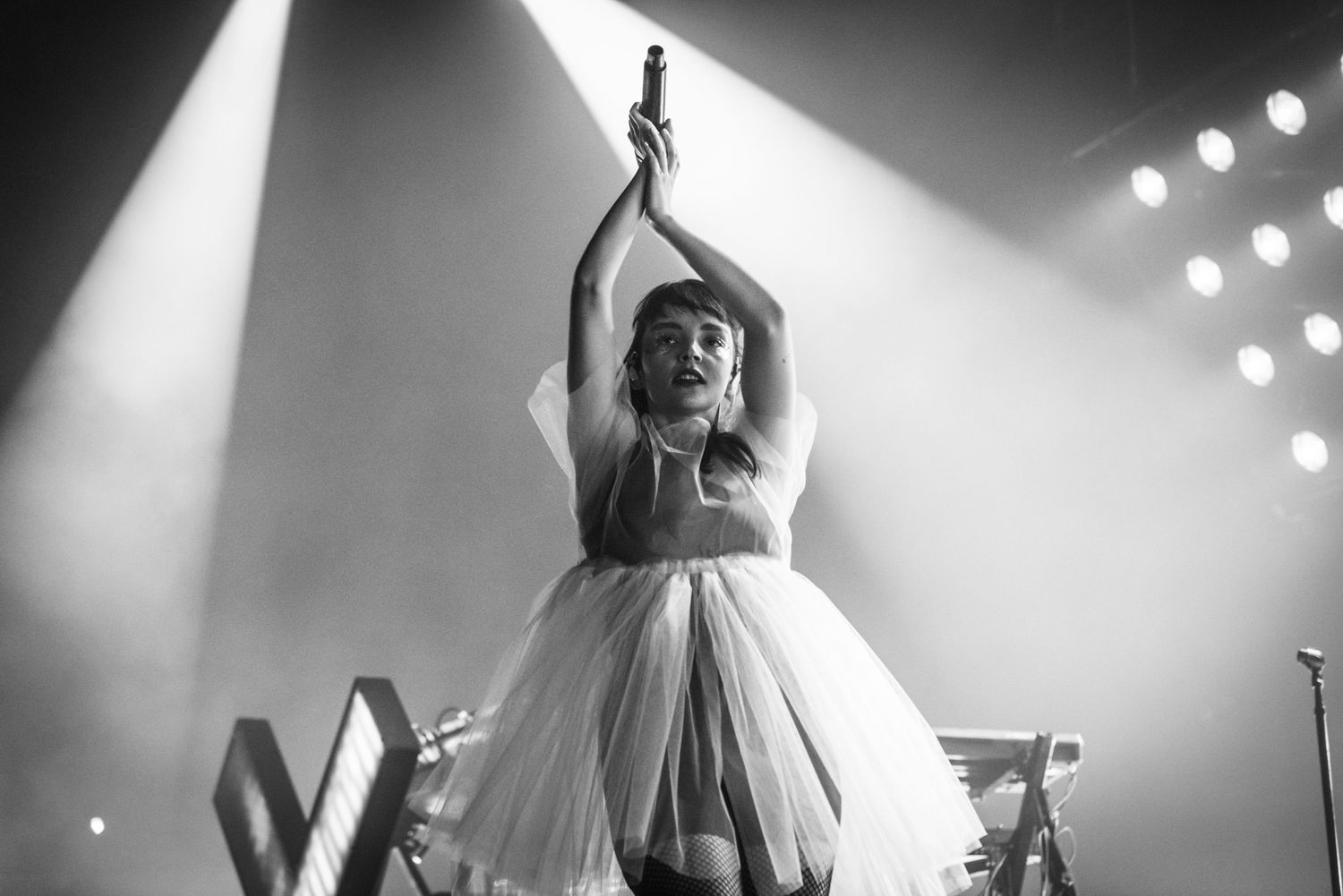 Performer in white tulle dress dances with arms raised under dramatic stage lighting.