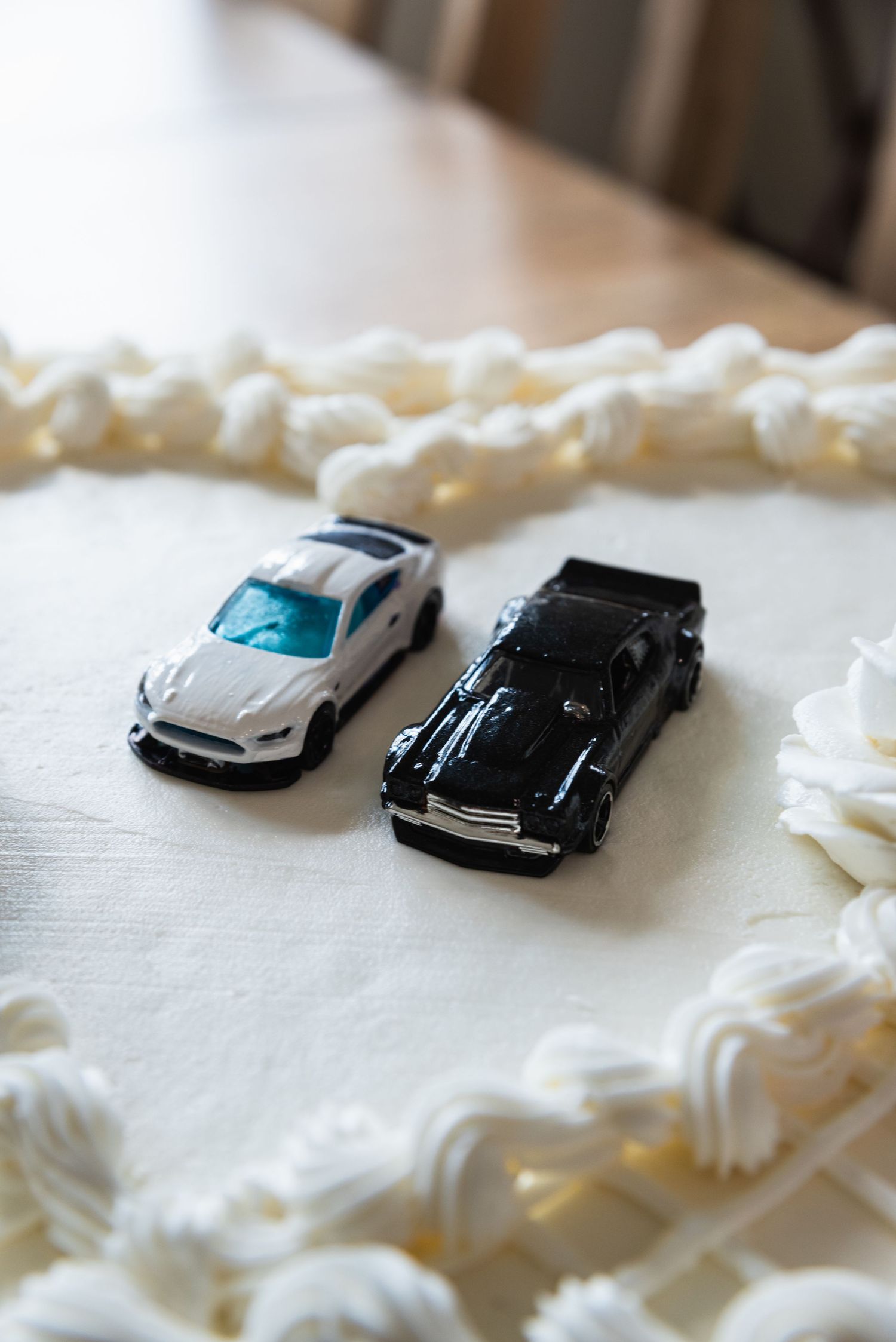 Close-up of vintage toy cars decorating a white wedding cake with piped frosting border.