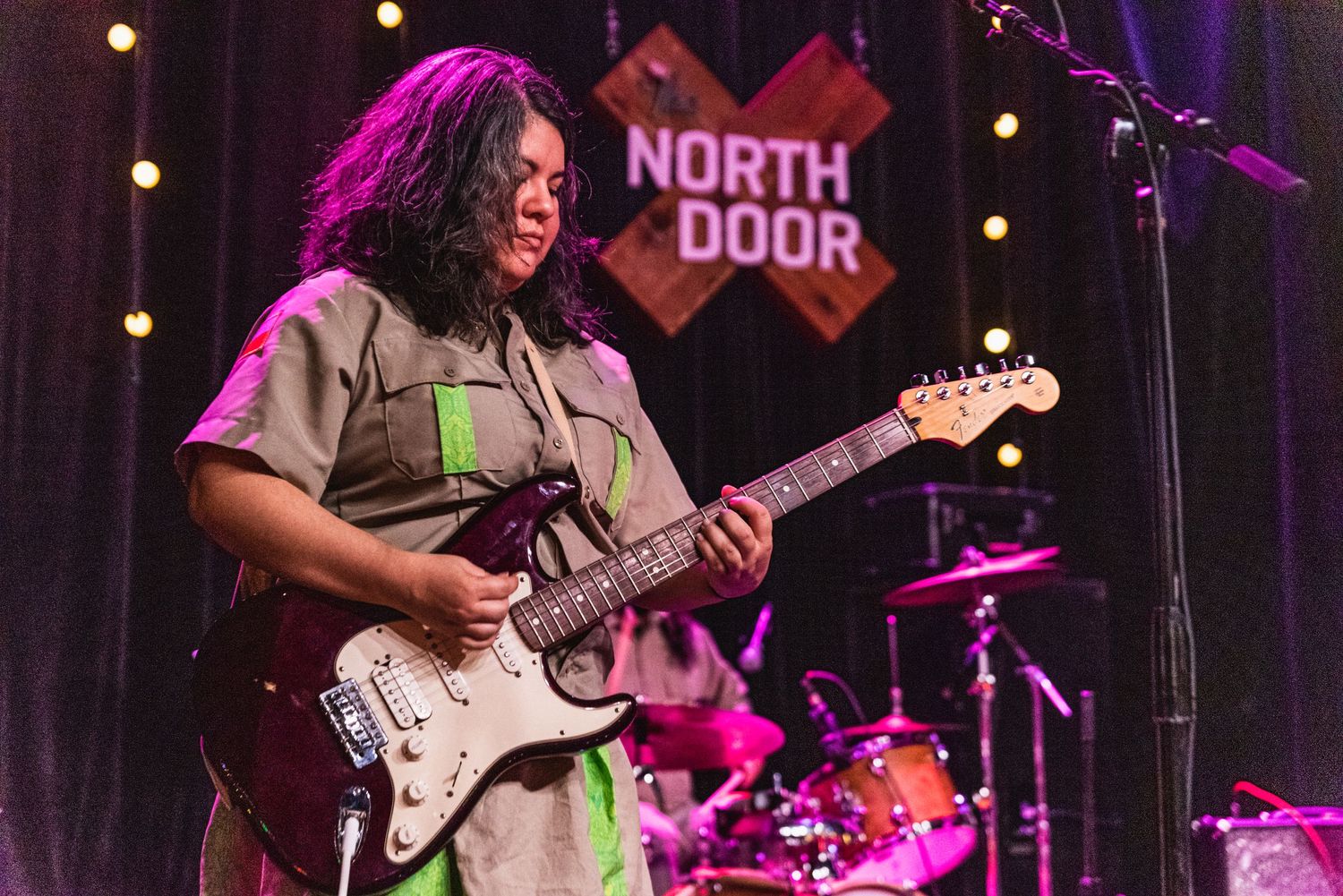 Guitar player performing on stage at North Door music venue with string instruments and drums.