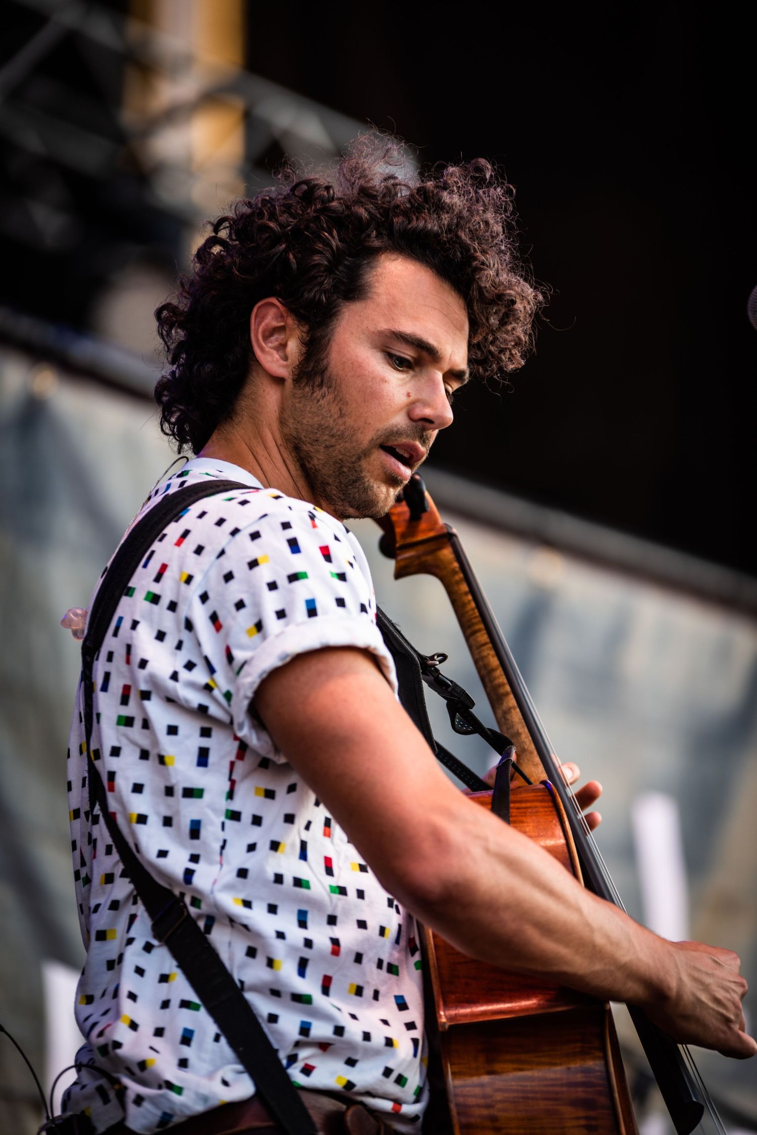 Musician in polka dot shirt plays cello passionately during outdoor performance.