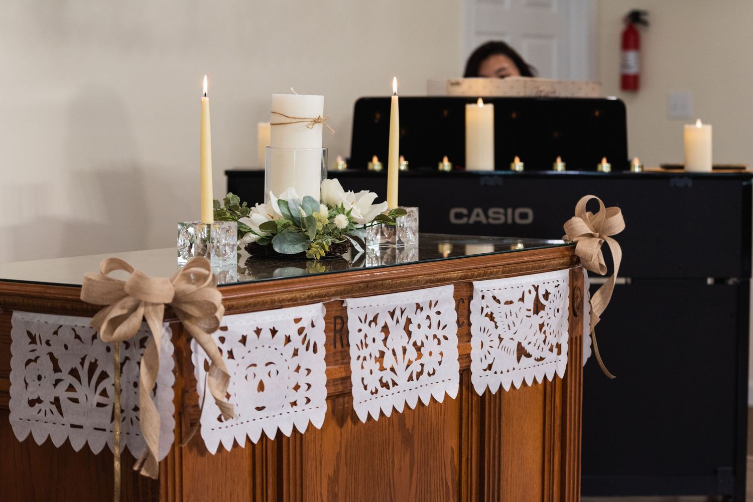 White lace bunting and decorative candles adorn a wooden piano with a Casio keyboard at a wedding venue.