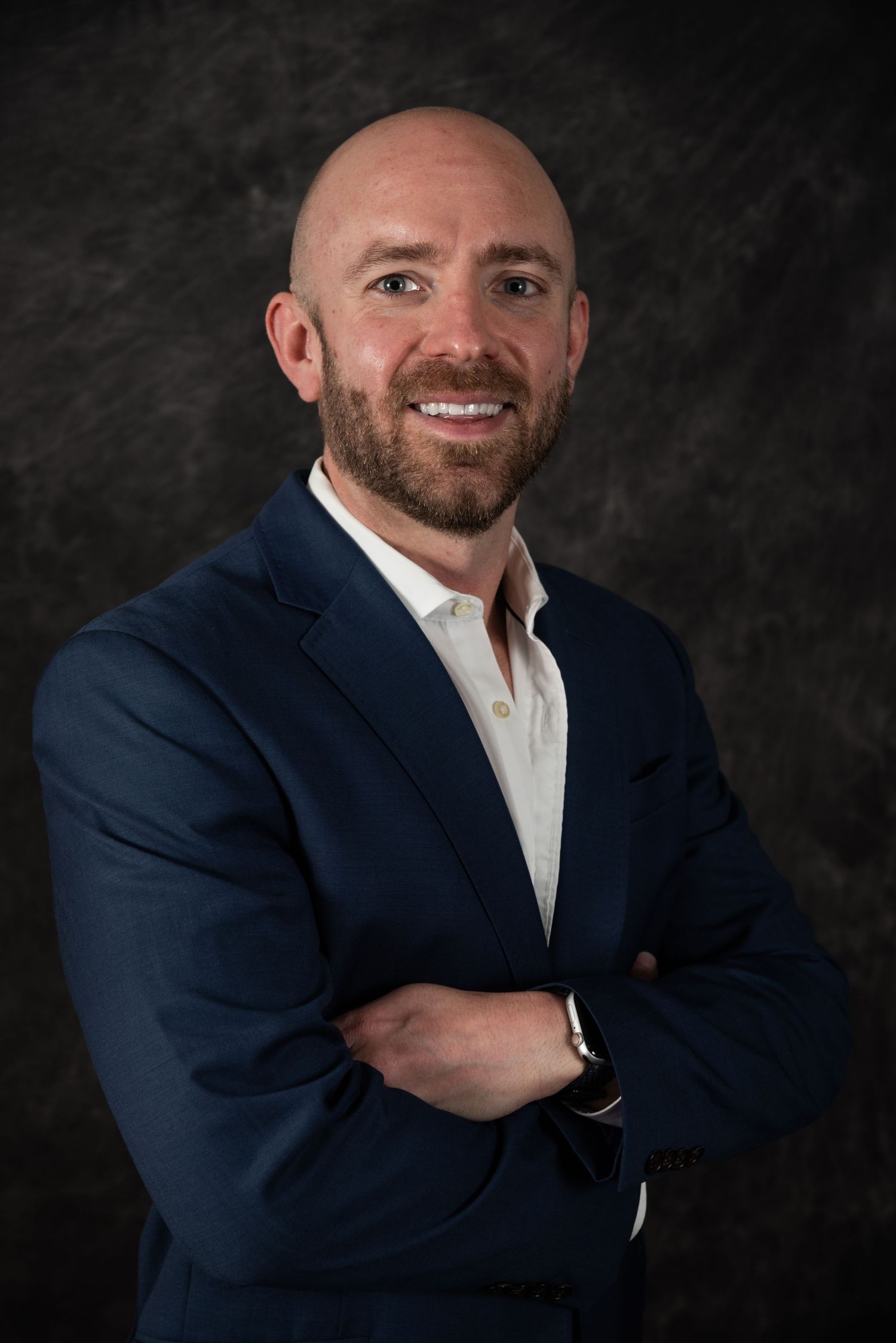Business headshot of person in dark suit jacket with arms crossed showing confident pose.