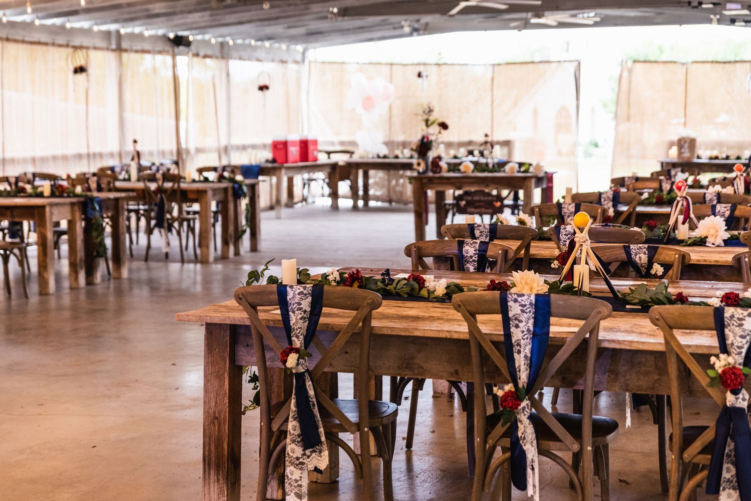 A large reception hall set up with wooden farm tables and chairs in an industrial style space.