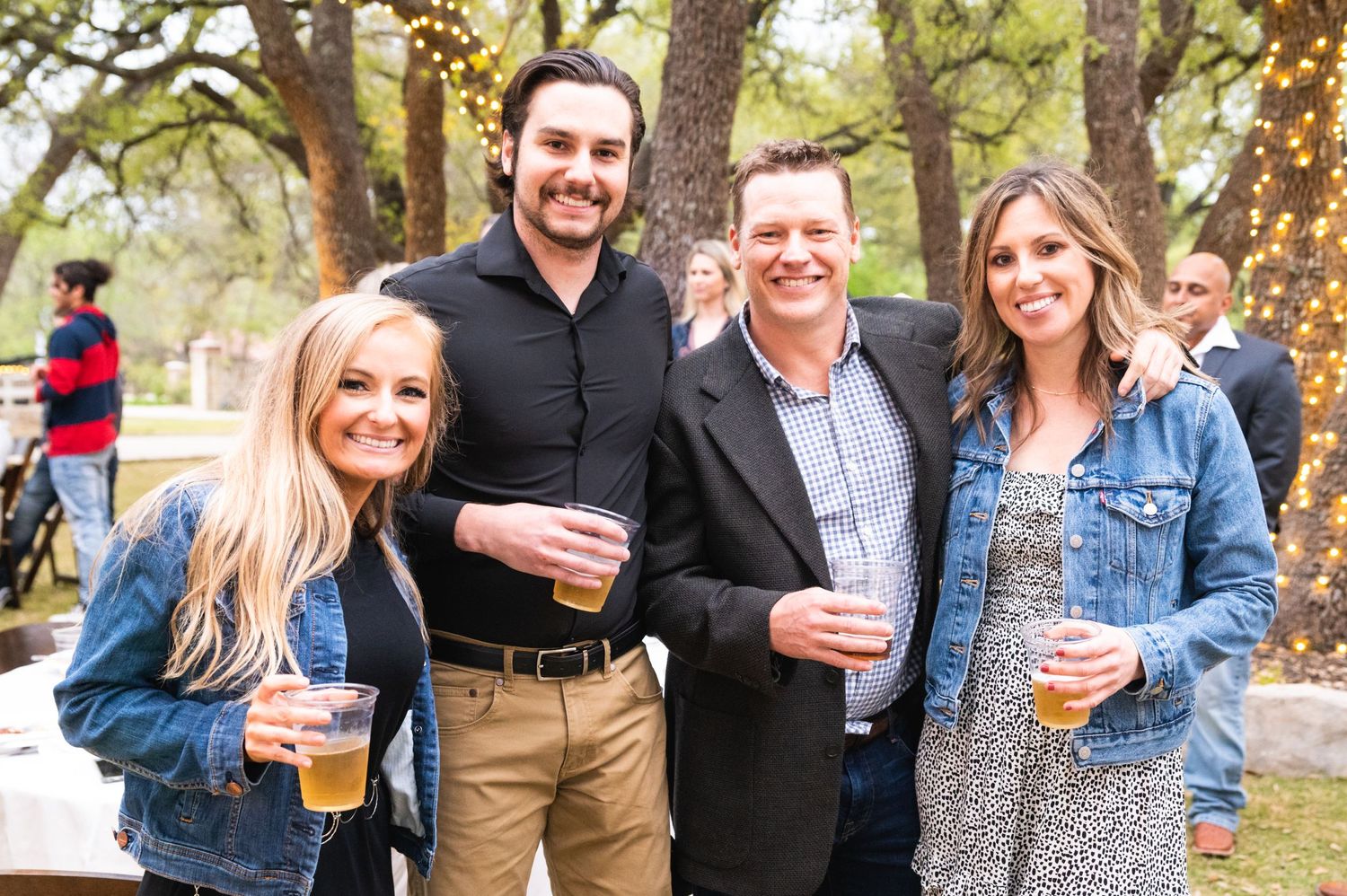 Group of friends enjoying drinks at an outdoor gathering under trees.