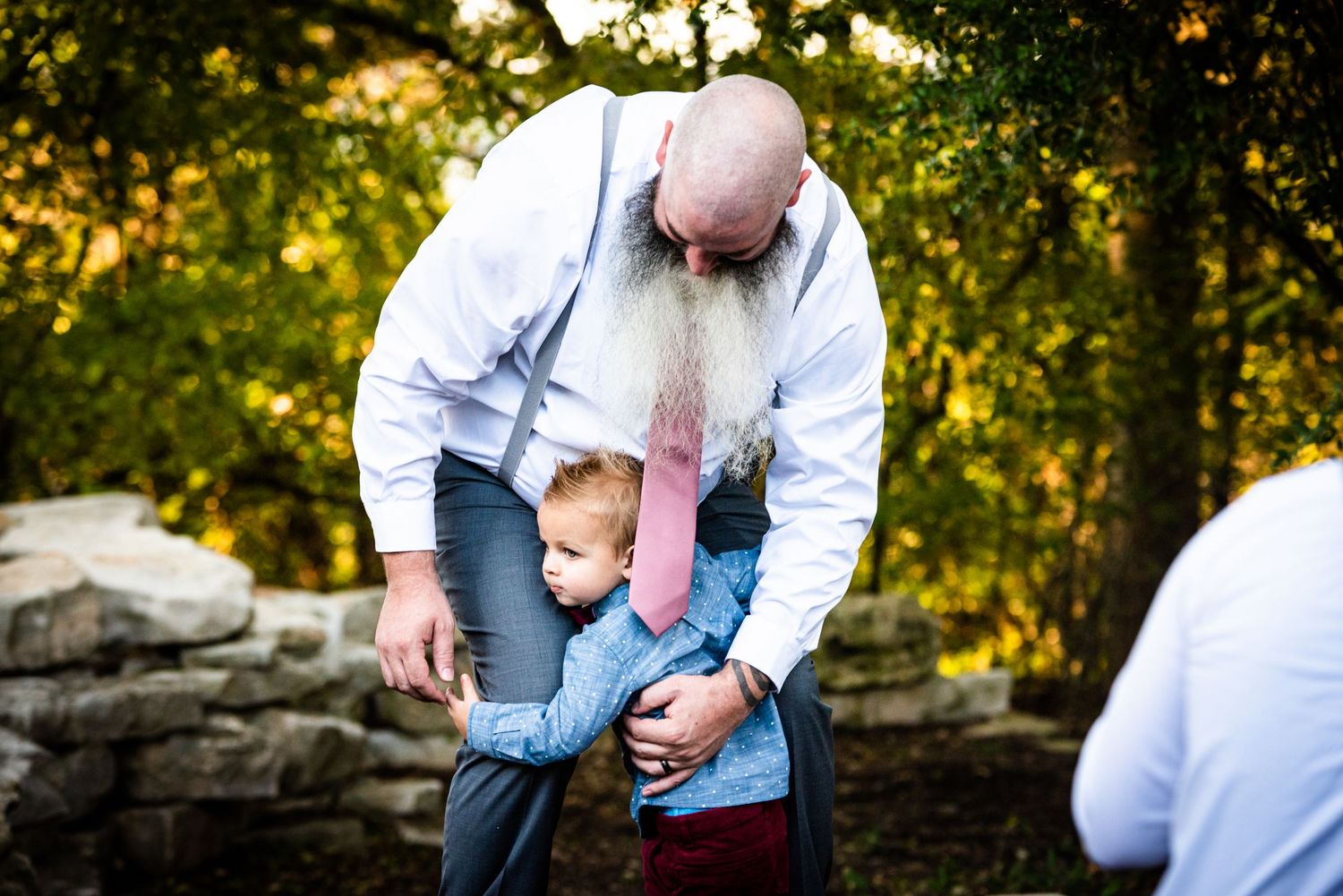 Tender moment between adult and small child at outdoor wedding venue.