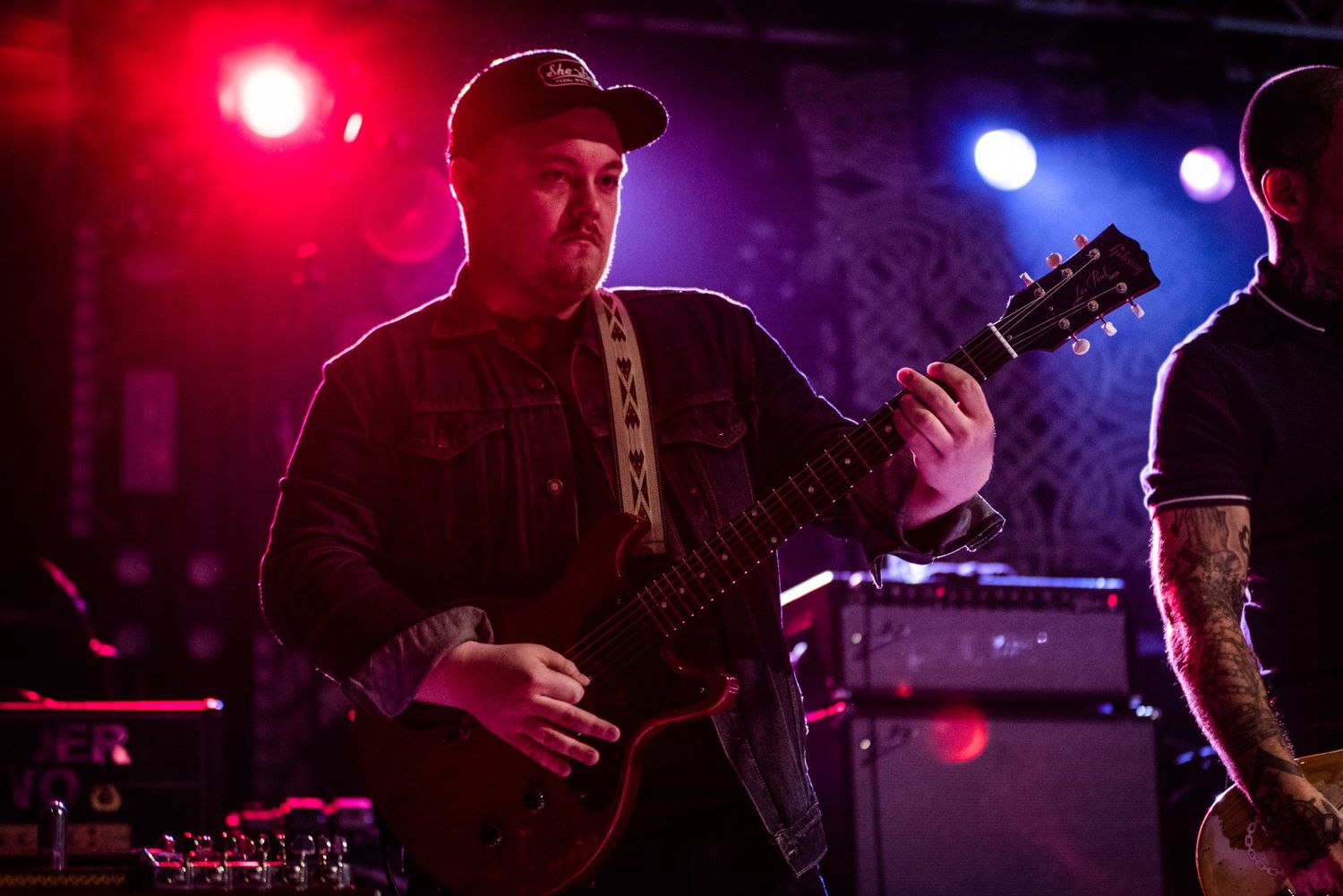 Guitarist performing under red and blue stage lights during rock concert.