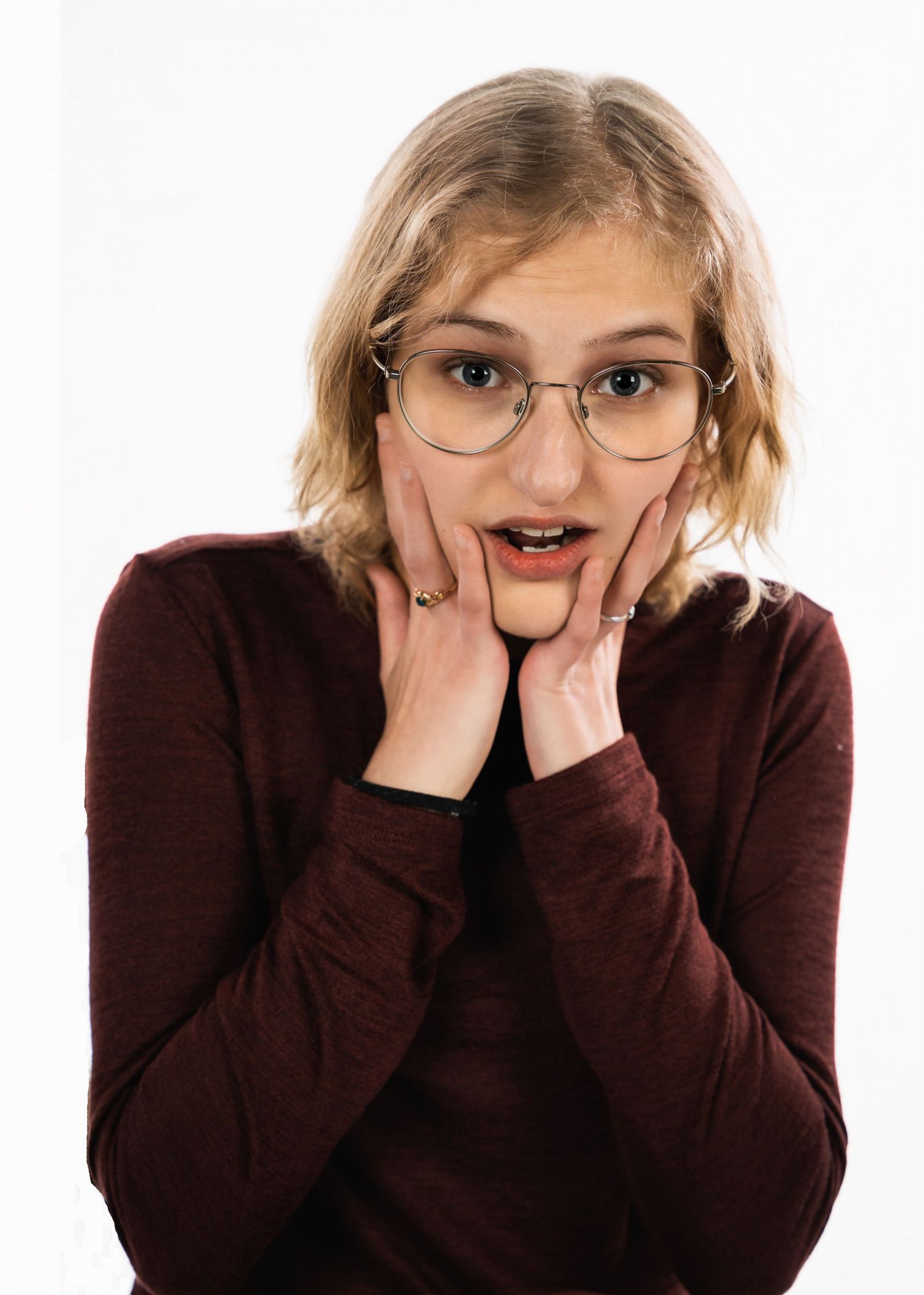 A person wearing glasses and a burgundy sweater shows an excited expression with hands on cheeks.