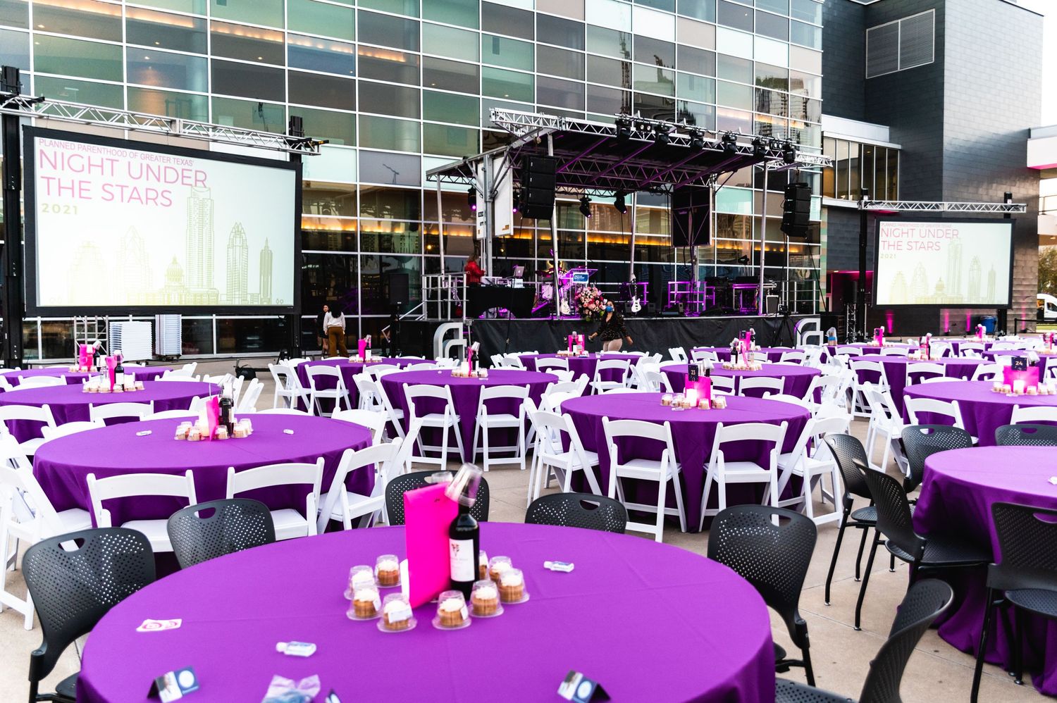 Large event space setup with purple tablecloths and white chairs for formal gathering.