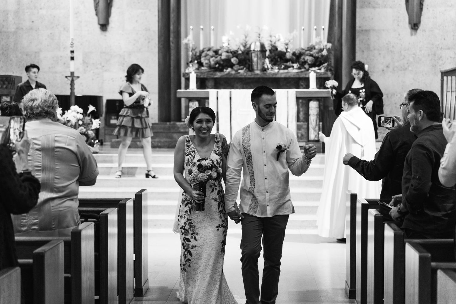 A black and white photo captures a joyful couple walking down the church aisle after their ceremony.