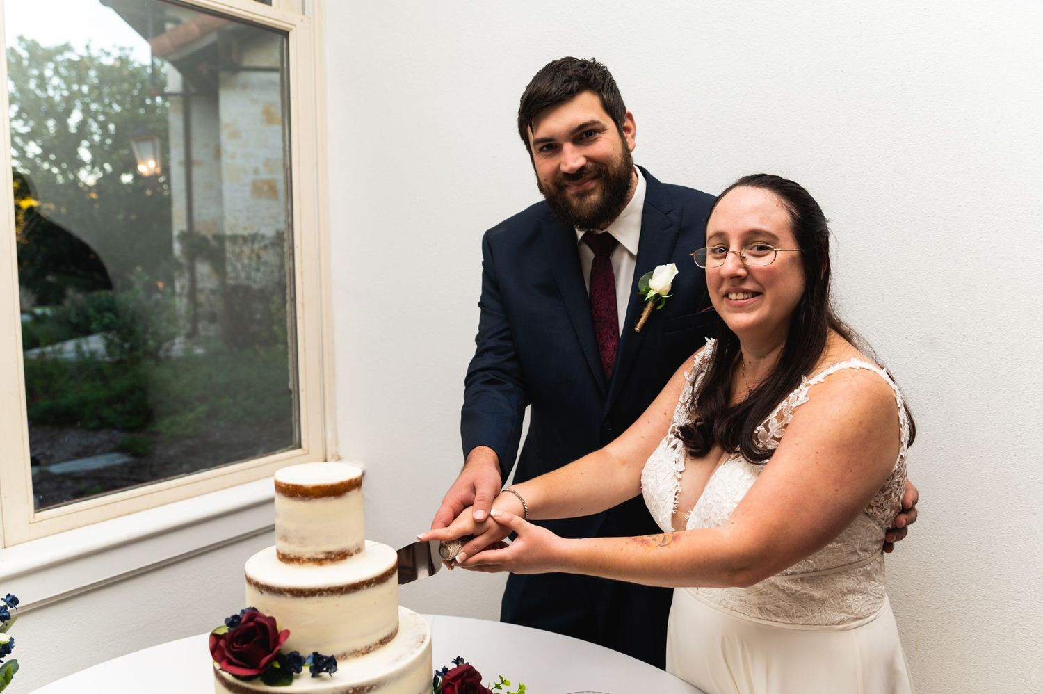 A wedding couple cuts into their modern semi-naked tiered cake together.