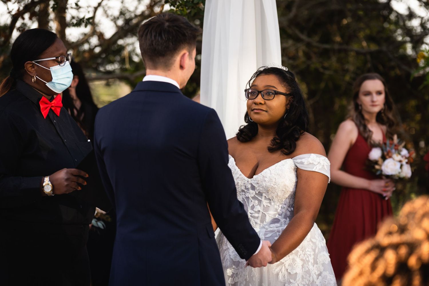 Wedding ceremony taking place outdoors with couple exchanging vows under an arch.