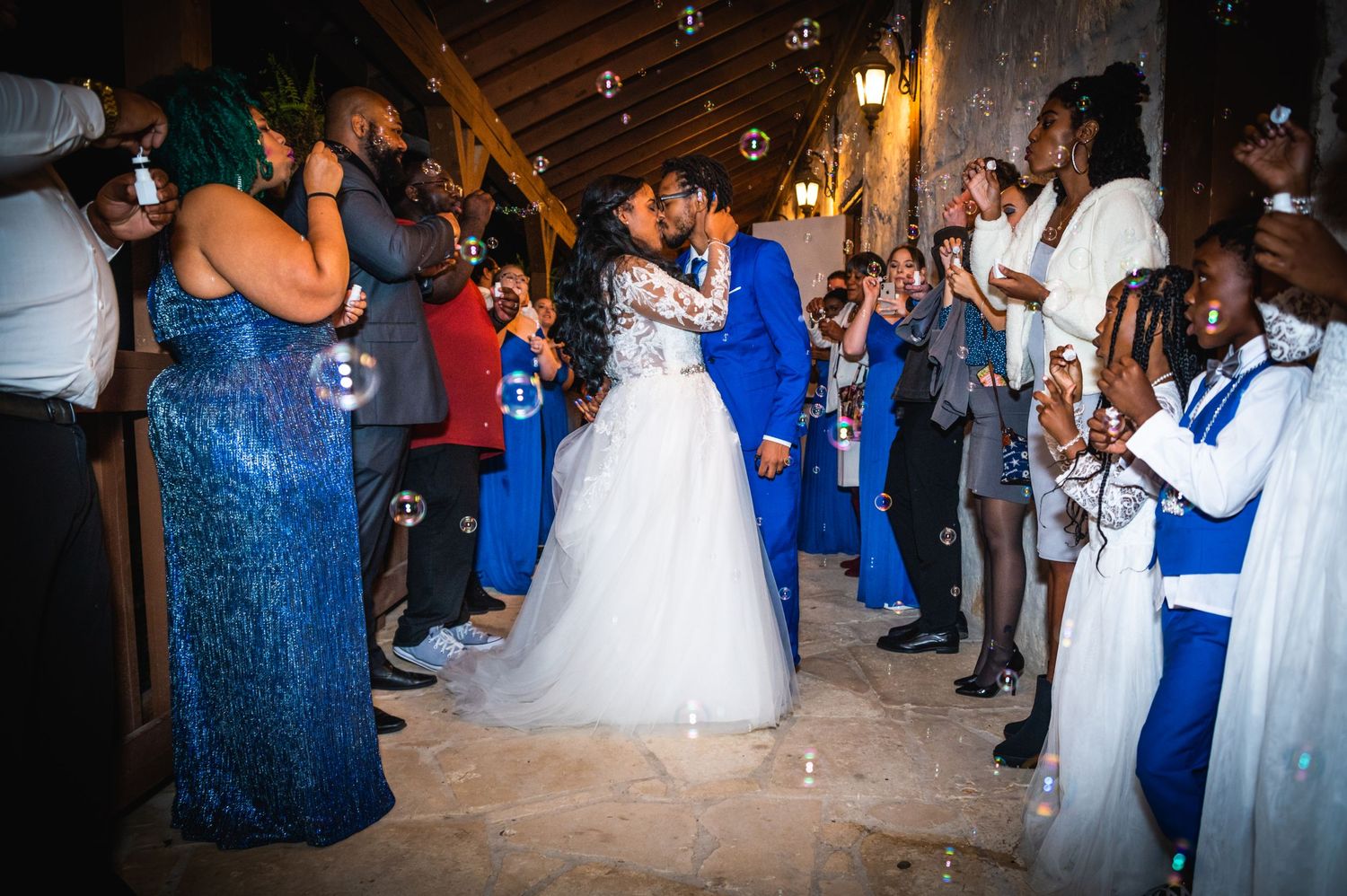 Wedding reception dance with guests in blue attire blowing bubbles around dancing couple.
