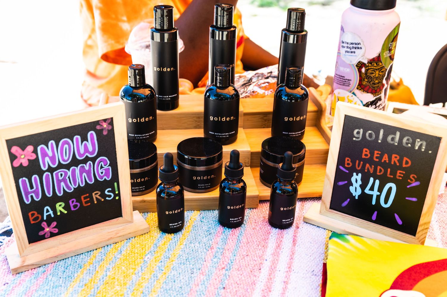 Display of beauty products and price signs on a colorful rainbow tablecloth.