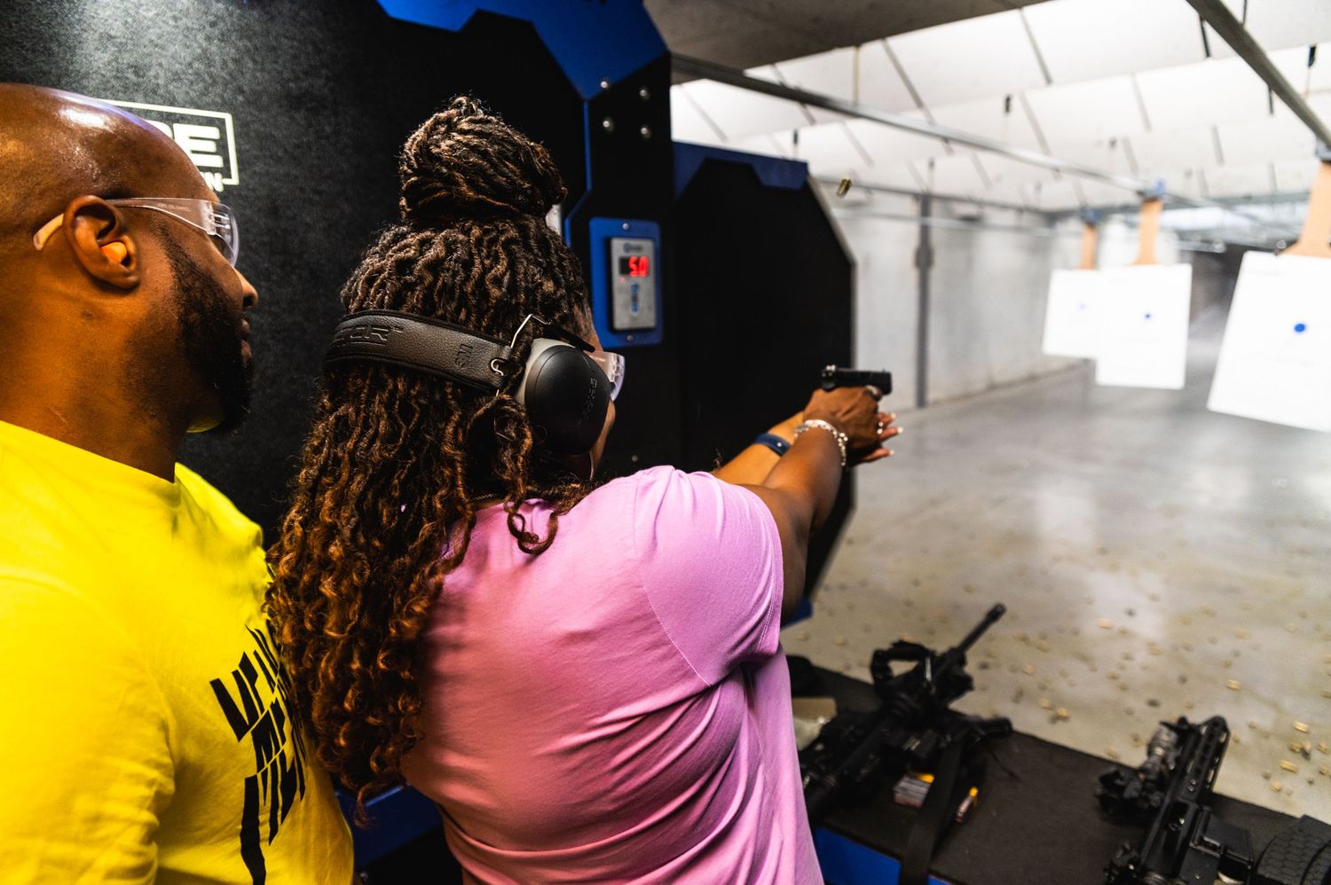Two shooters practicing at an indoor firing range wearing ear protection.