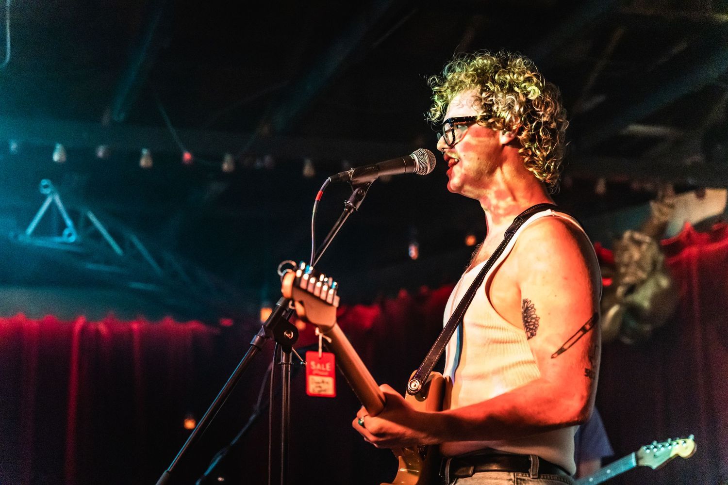 Performer singing and playing guitar on stage with colorful lighting effects.