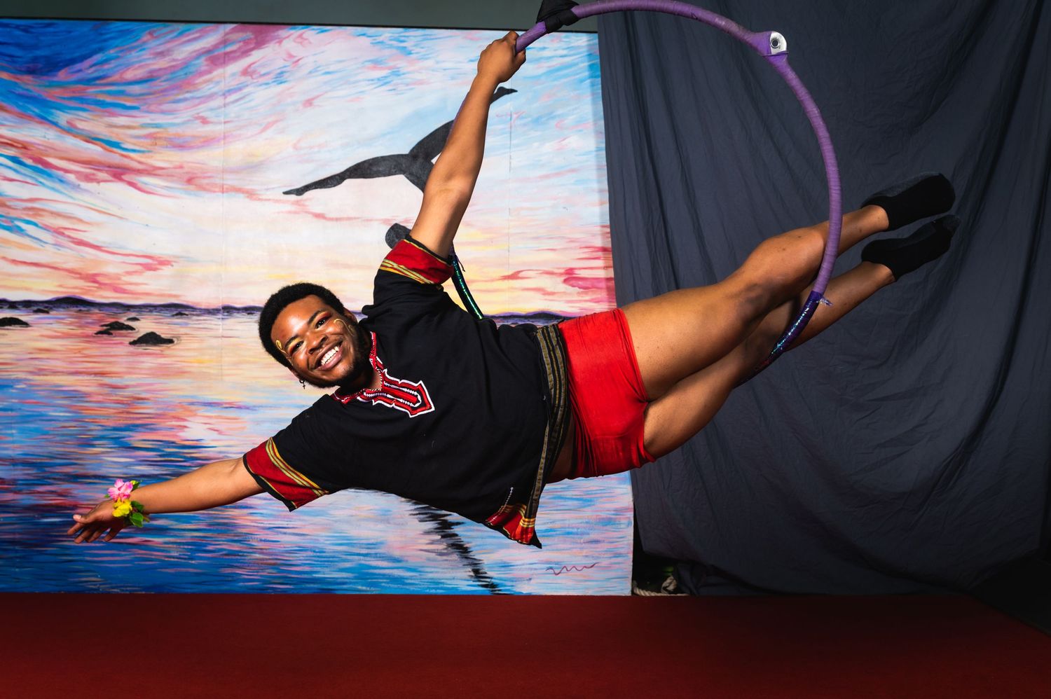 Aerial performer strikes dynamic pose while suspended in air against colorful backdrop.