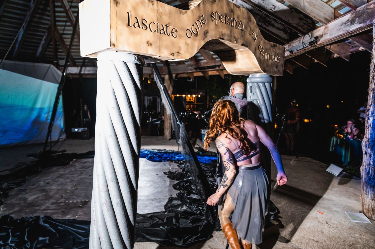 Performers move through rustic venue space with wooden beams and lighting equipment.