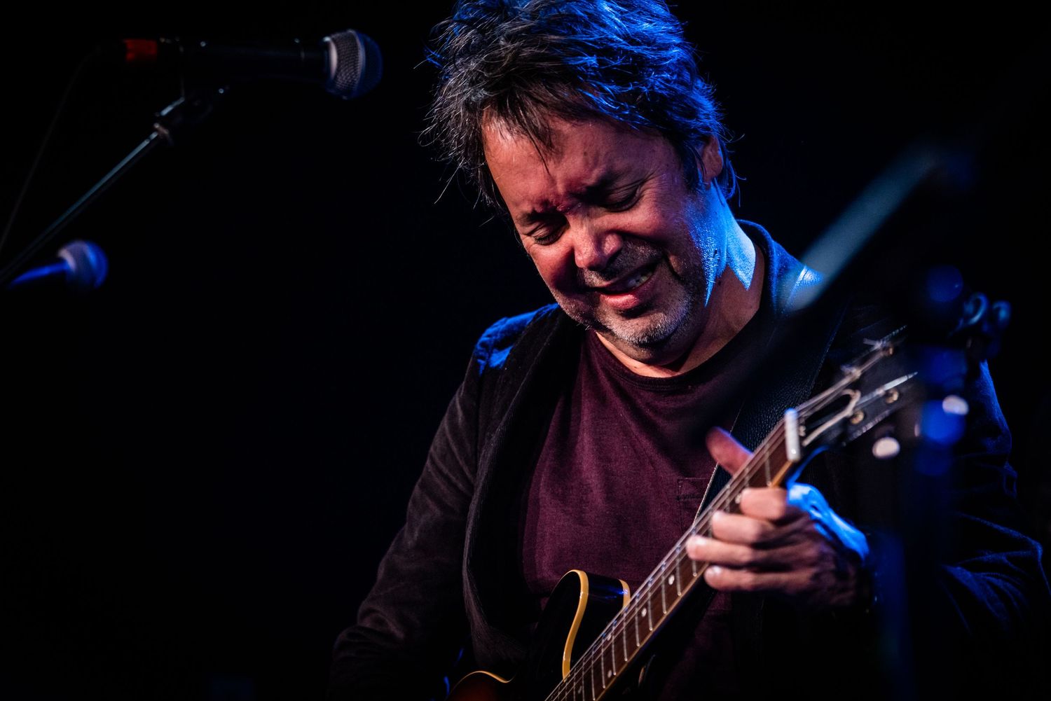 Guitarist plays electric guitar under dramatic blue stage lighting during performance.