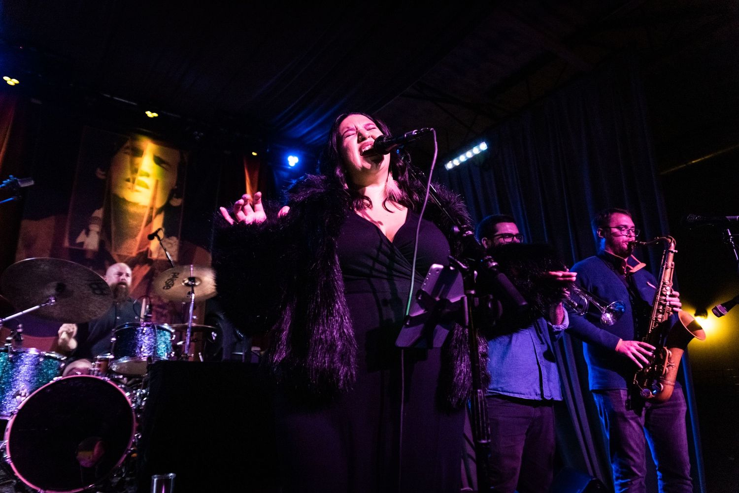 A band performs on stage with brass section under dramatic lighting.