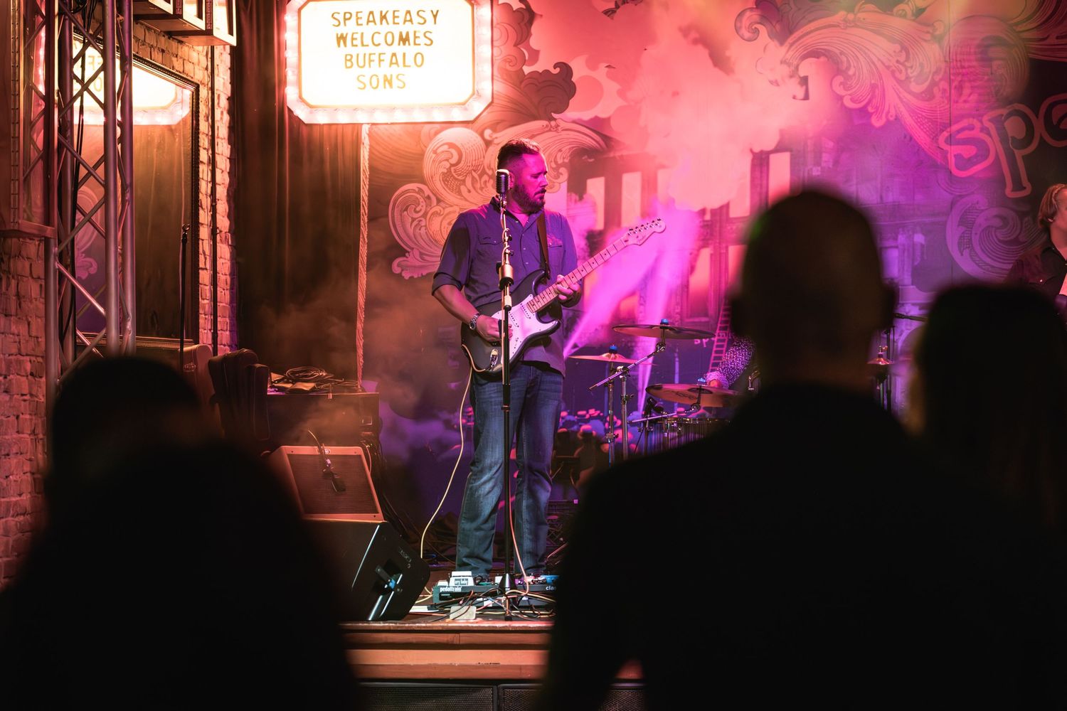 Guitarist performs on stage through atmospheric smoke and colored lighting.