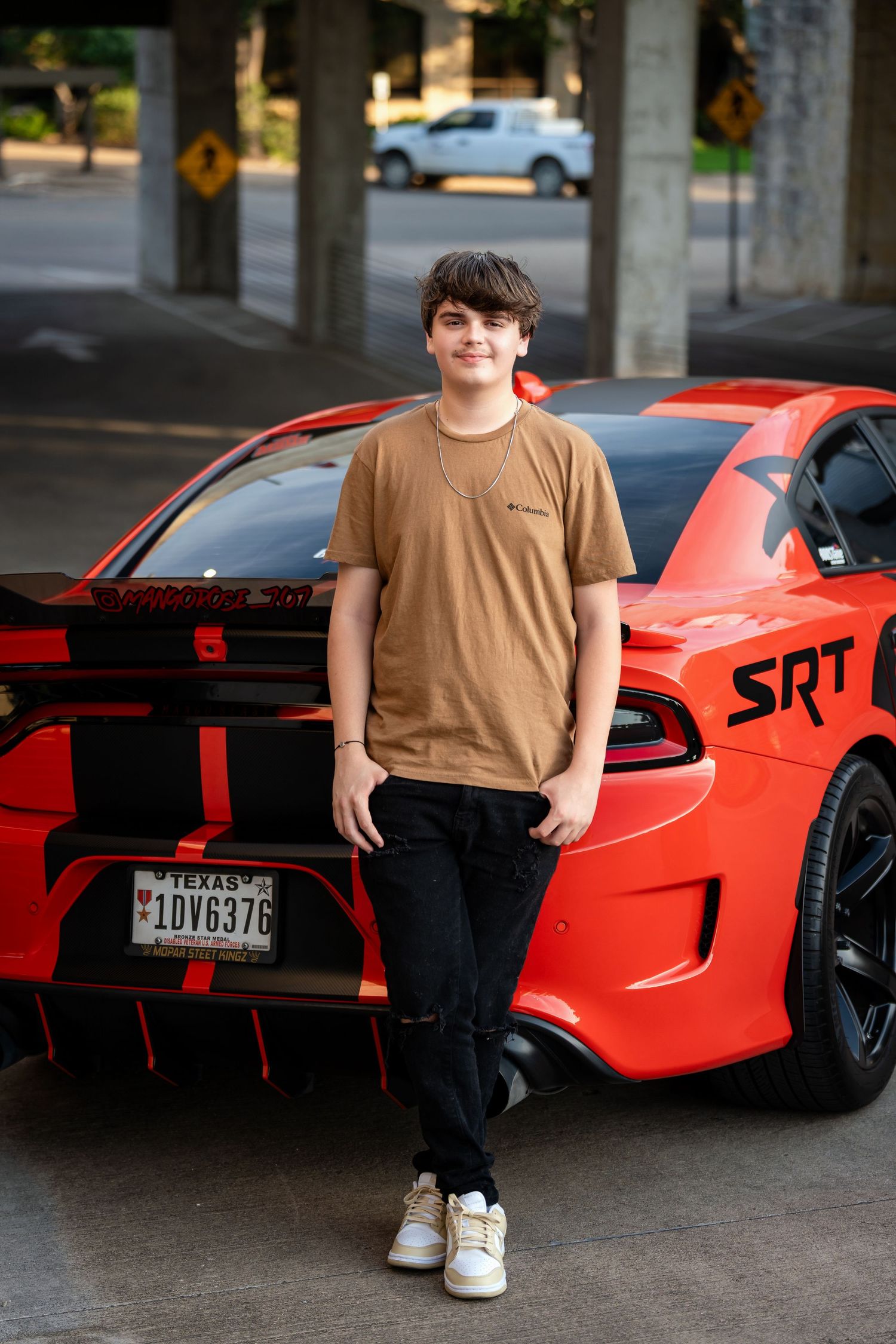 A portrait beside a red Dodge Charger SRT with black racing stripes in a parking structure.