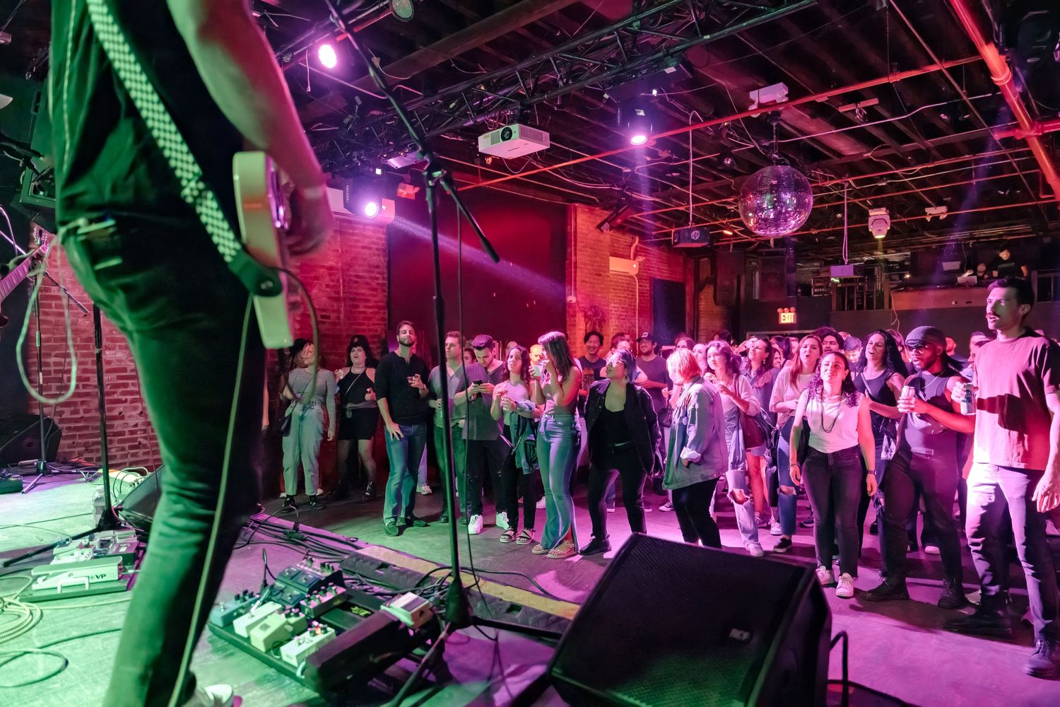 Crowd watches live band performance in venue with red and green lighting effects.