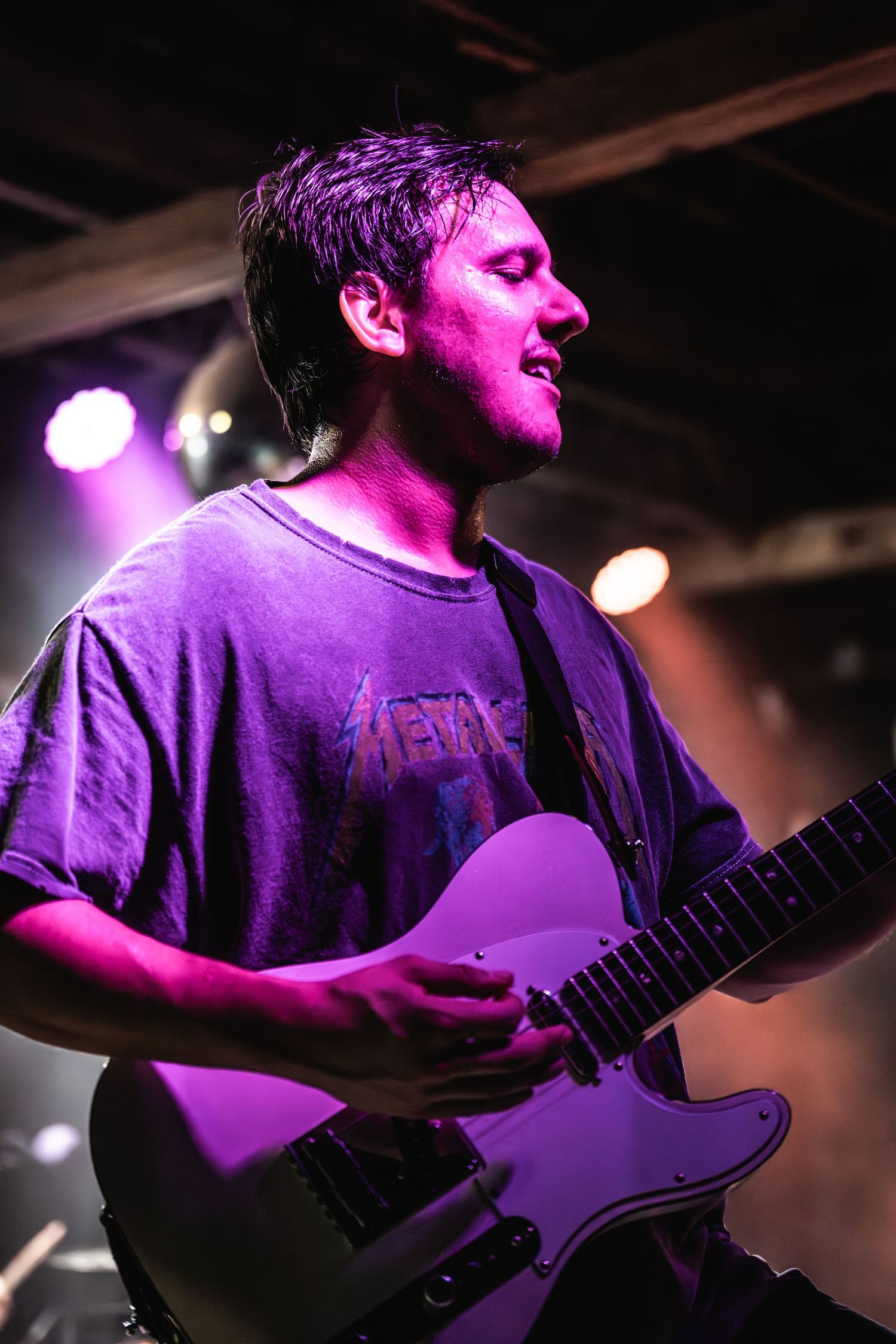Guitarist performs under purple stage lighting during intimate concert venue show.