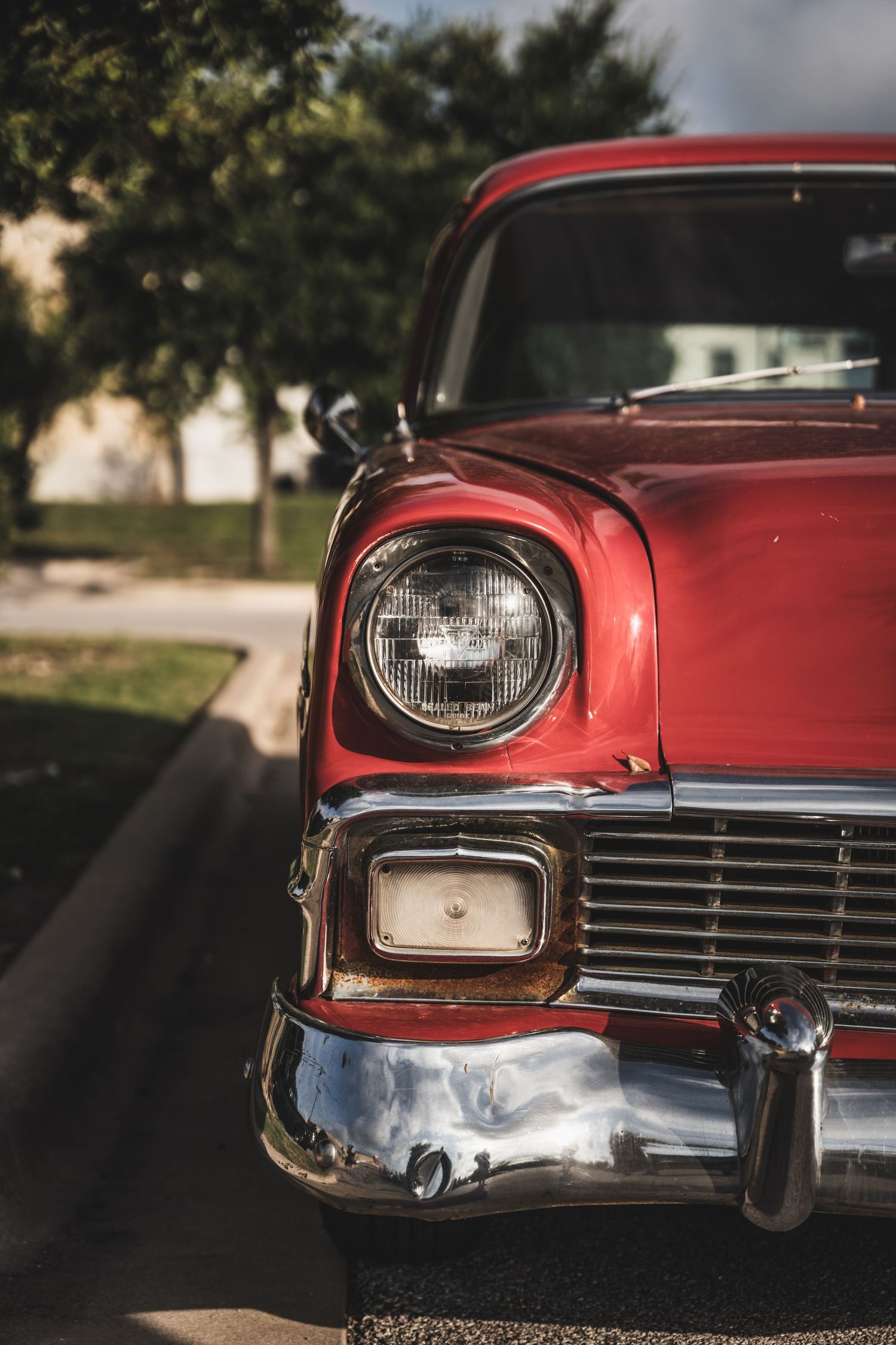 Close-up of a classic red Chevrolet's front headlight and chrome grille.