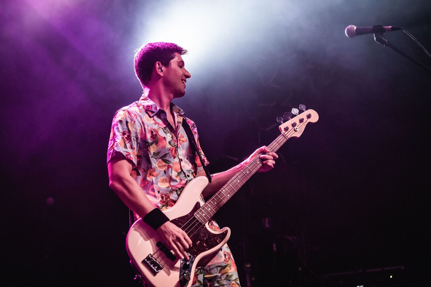 Bass player in floral shirt performs under dramatic stage lighting.