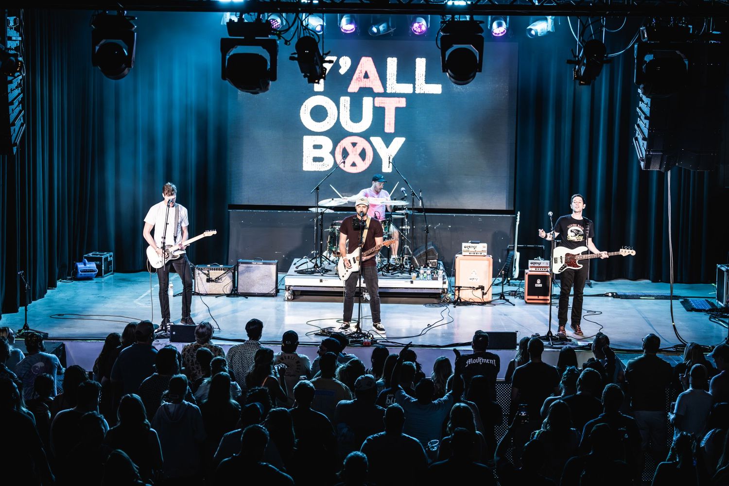 Band performs live set on stage with blue lighting and Y'ALL OUT BOY backdrop.