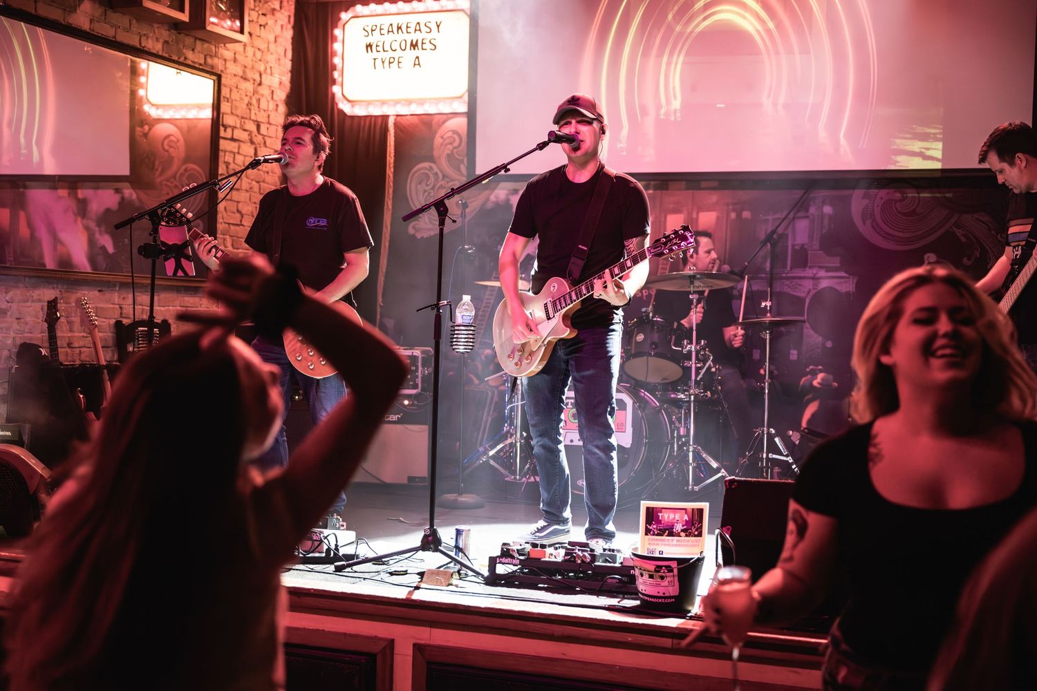 Rock band performing on stage while crowd watches at a small music venue.